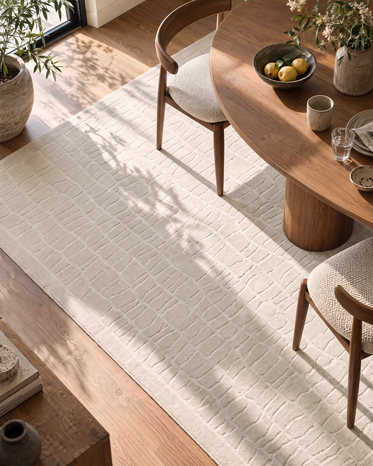 An ivory luxury Wilton jacquard area rug with a raised block texture adds sculptural softness and refined dimension to a wide modern living room with a cream sectional sofa, arched doorway, curated artwork, and warm natural light.