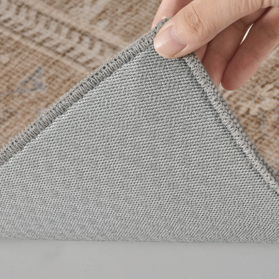 A close-up view of a beige vintage washable area rug shows its folded corner, gray non-slip backing, tightly woven construction, and neatly finished edge, highlighting practical durability and everyday comfort for living rooms and bedrooms.