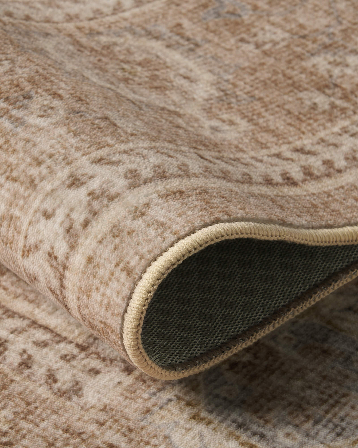 A close-up of a beige vintage washable area rug highlights its softly textured pile, distressed floral pattern, flexible folded edge, and dark non-slip woven backing, combining everyday comfort with refined craftsmanship for living rooms and bedrooms.