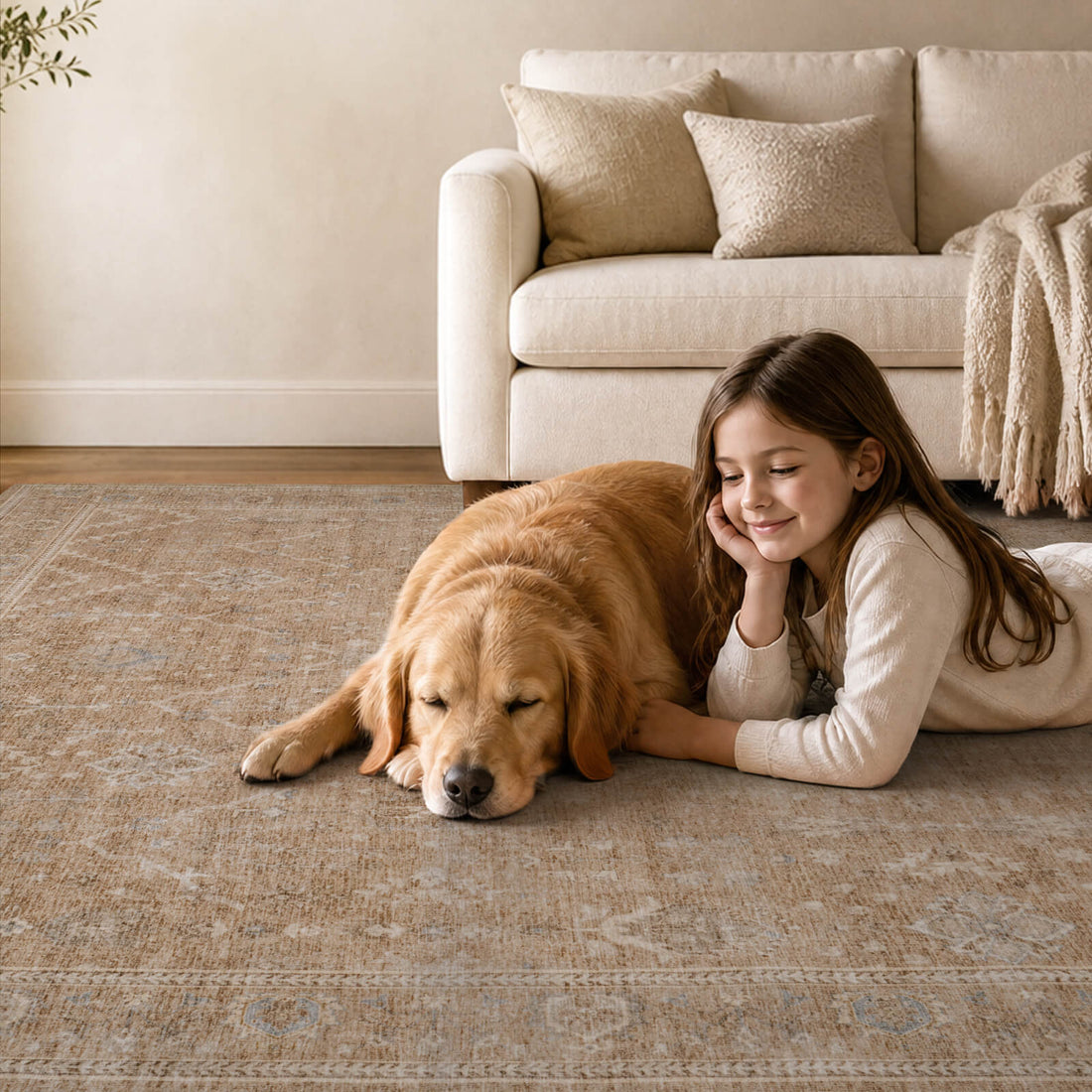 A beige vintage washable area rug with a softly distressed floral pattern provides a comfortable space for a young girl and her golden retriever to relax together, adding warmth and family-friendly charm to a cozy living room with a cream sofa and neutral decor.