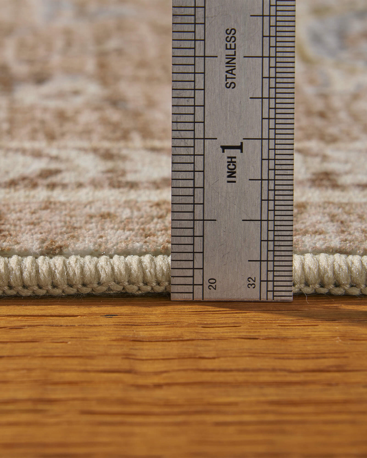 A close-up view of a beige vintage washable area rug shows its ruler-measured pile height, soft low-pile surface, and neatly bound edge, highlighting its comfortable texture and refined construction for living rooms, bedrooms, and everyday home use.