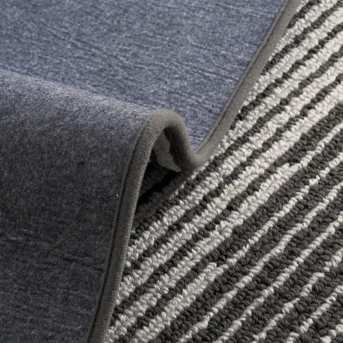 A close-up of black and white striped woven stair treads highlights their raised ribbed texture, soft woven surface, flexible non-slip backing, and neatly bound edges, showcasing comfortable footing, durable construction, and practical protection for indoor wooden stairs.