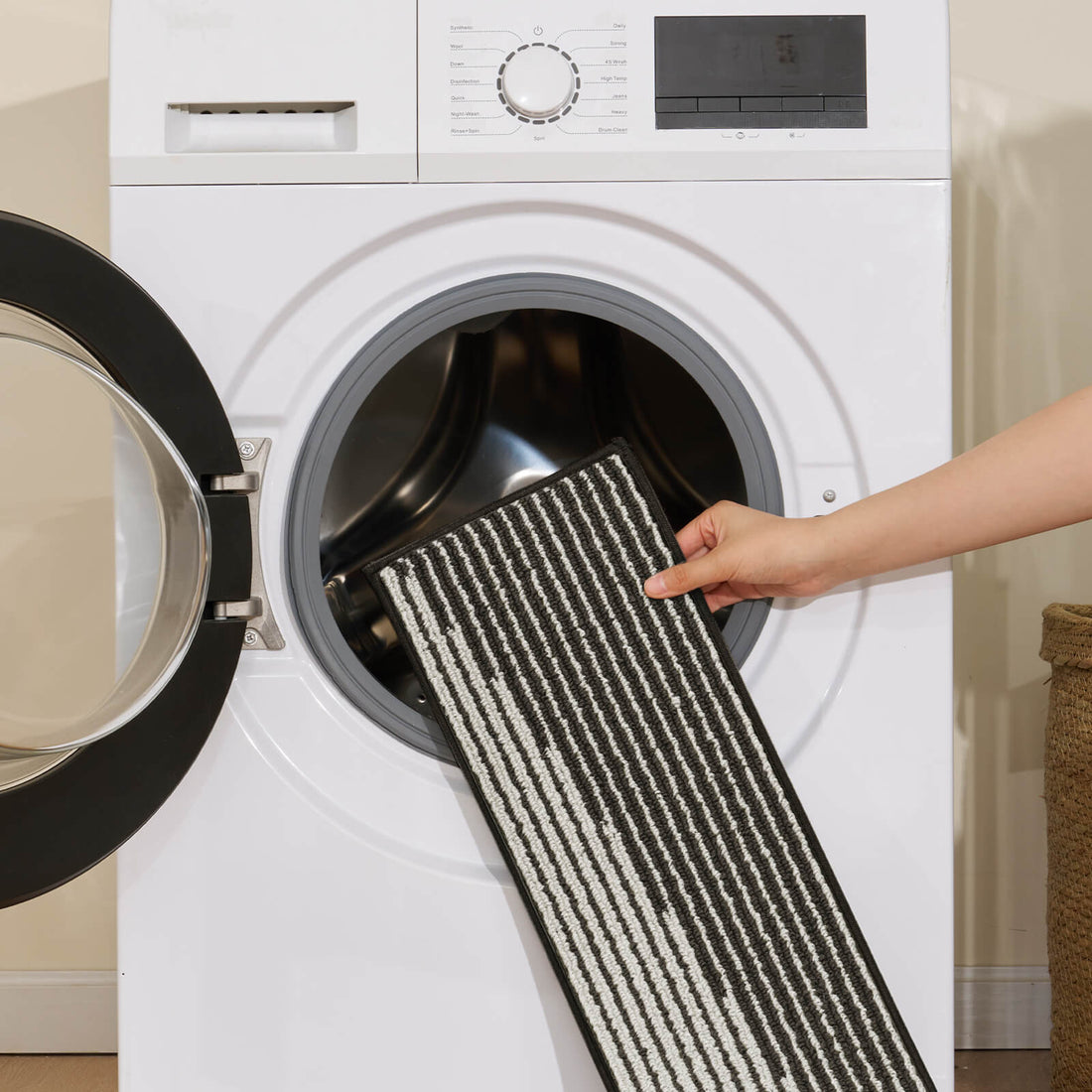 A black and white striped woven stair tread mat is shown being placed into a front-loading washing machine, highlighting its machine-washable design, textured woven surface, and easy-care convenience for keeping indoor stairs clean, comfortable, and stylish.