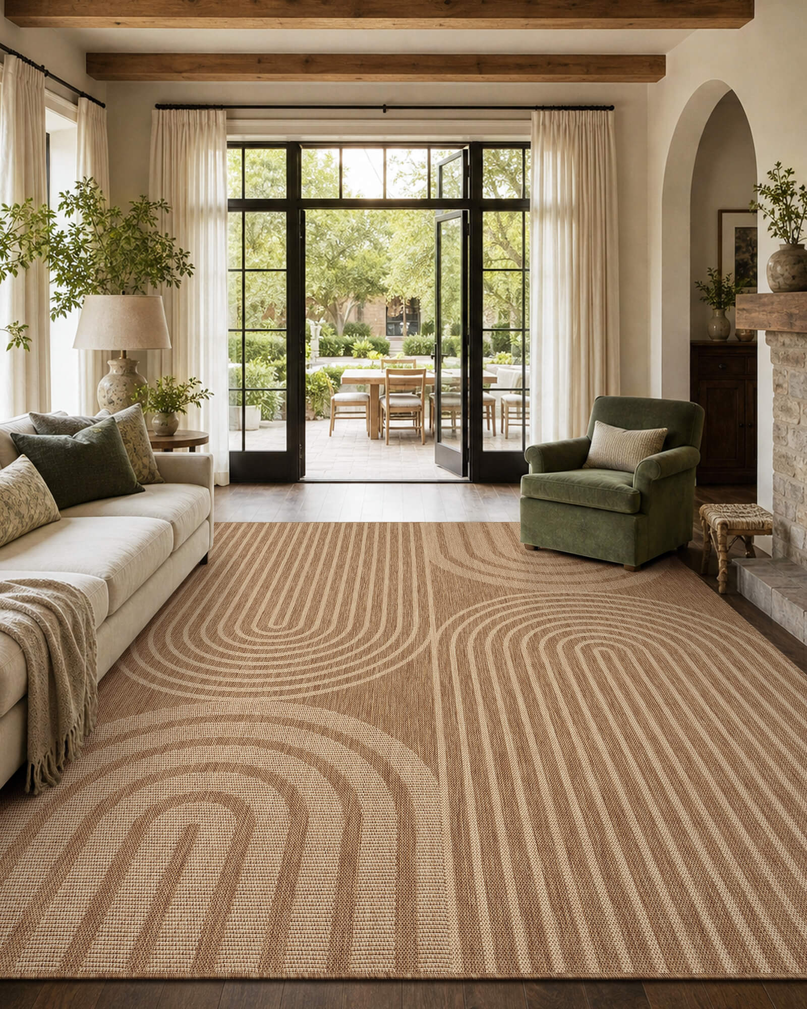 A brown abstract indoor outdoor area rug with a modern arched line pattern adds warm texture to a French door living room with a cream sofa, green accent chair, wood beams, and relaxed farmhouse decor.