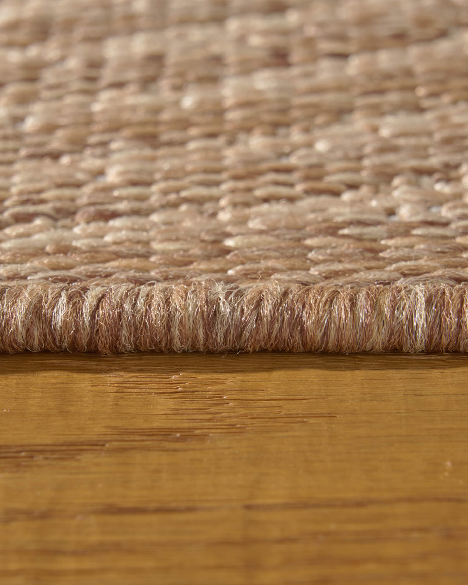 A close-up view of a brown abstract outdoor rug showing its low-profile edge, woven surface texture, and durable raised pattern for weather-resistant patio, deck, and porch use.