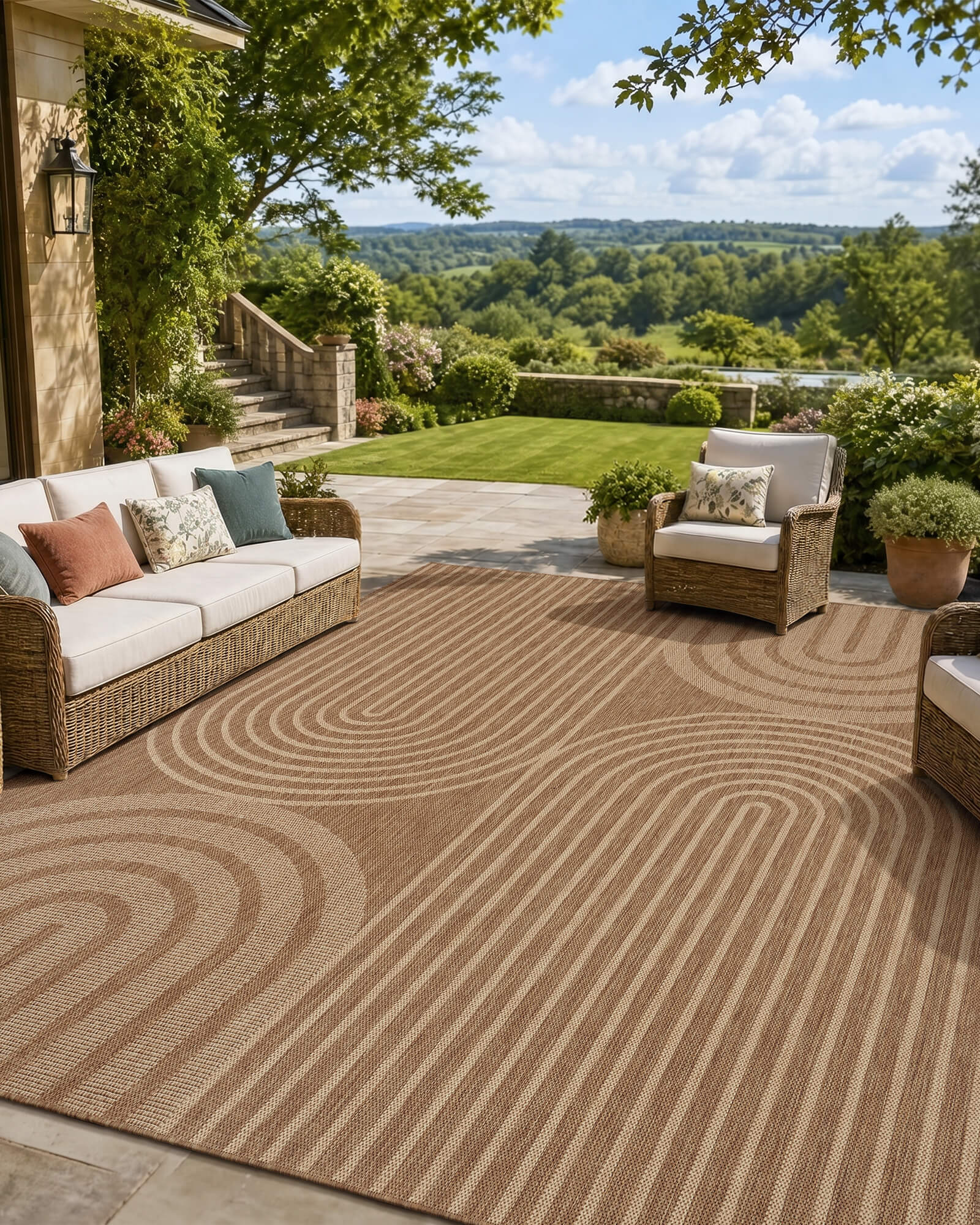 A brown abstract outdoor rug with a modern arched line pattern adds warm texture to a scenic patio lounge with wicker seating, garden greenery, open views, and weather-resistant outdoor style.