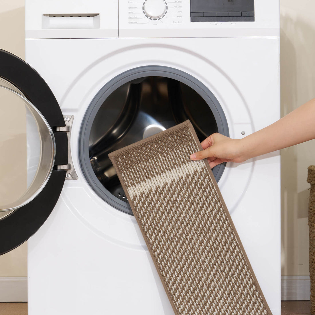 A brown gradient striped woven stair tread mat is shown being placed into a front-loading washing machine, highlighting its machine-washable design, soft raised woven texture, and modern ombre stripe pattern for easy-care comfort and practical protection on indoor wooden stairs.