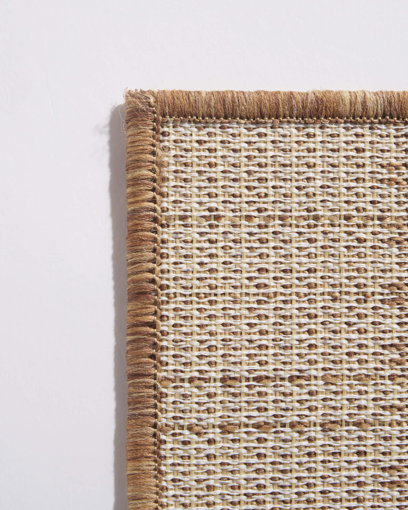A close-up of the back corner of a brown outdoor rug highlighting the woven backing, reinforced edge binding, and durable construction designed for patios, porches, decks, and high-traffic outdoor spaces.