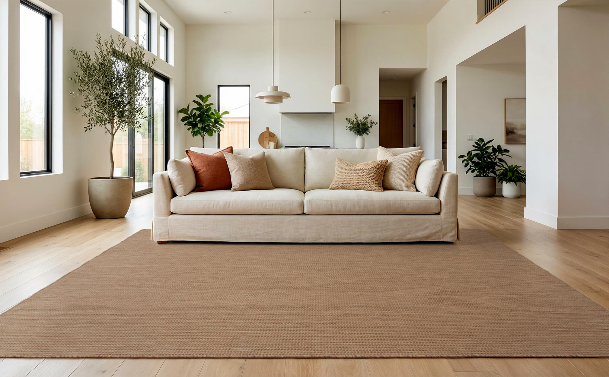 A brown plain weave indoor outdoor area rug adds warm natural texture to a bright living room with a cream sofa, wood floors, tall windows, indoor plants, and clean modern decor.