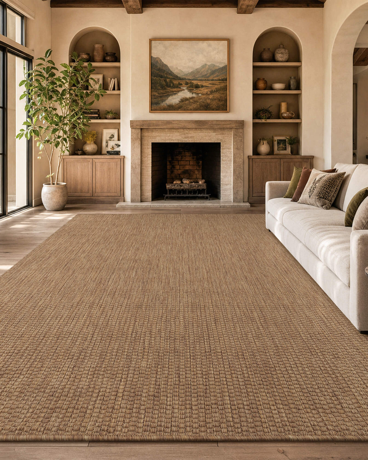 A brown plain weave indoor outdoor area rug adds natural jute-look texture to a cozy fireplace living room with a cream sofa, built-in shelves, wood beams, and warm farmhouse decor.