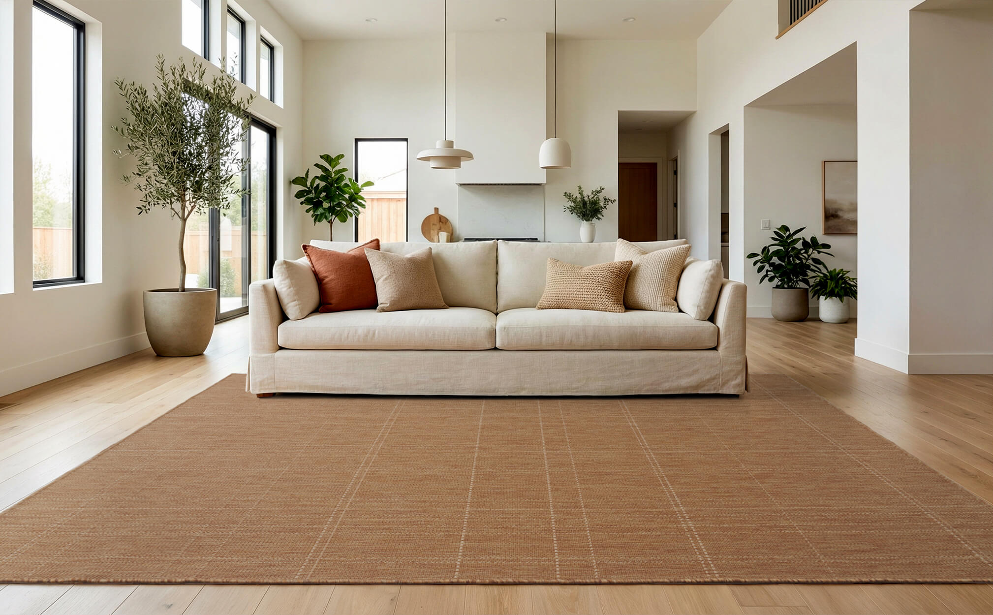A brown plain weave indoor outdoor area rug with a subtle check border adds warm natural texture to a modern living room with a cream sofa, tall windows, wood floors, and fresh neutral decor.