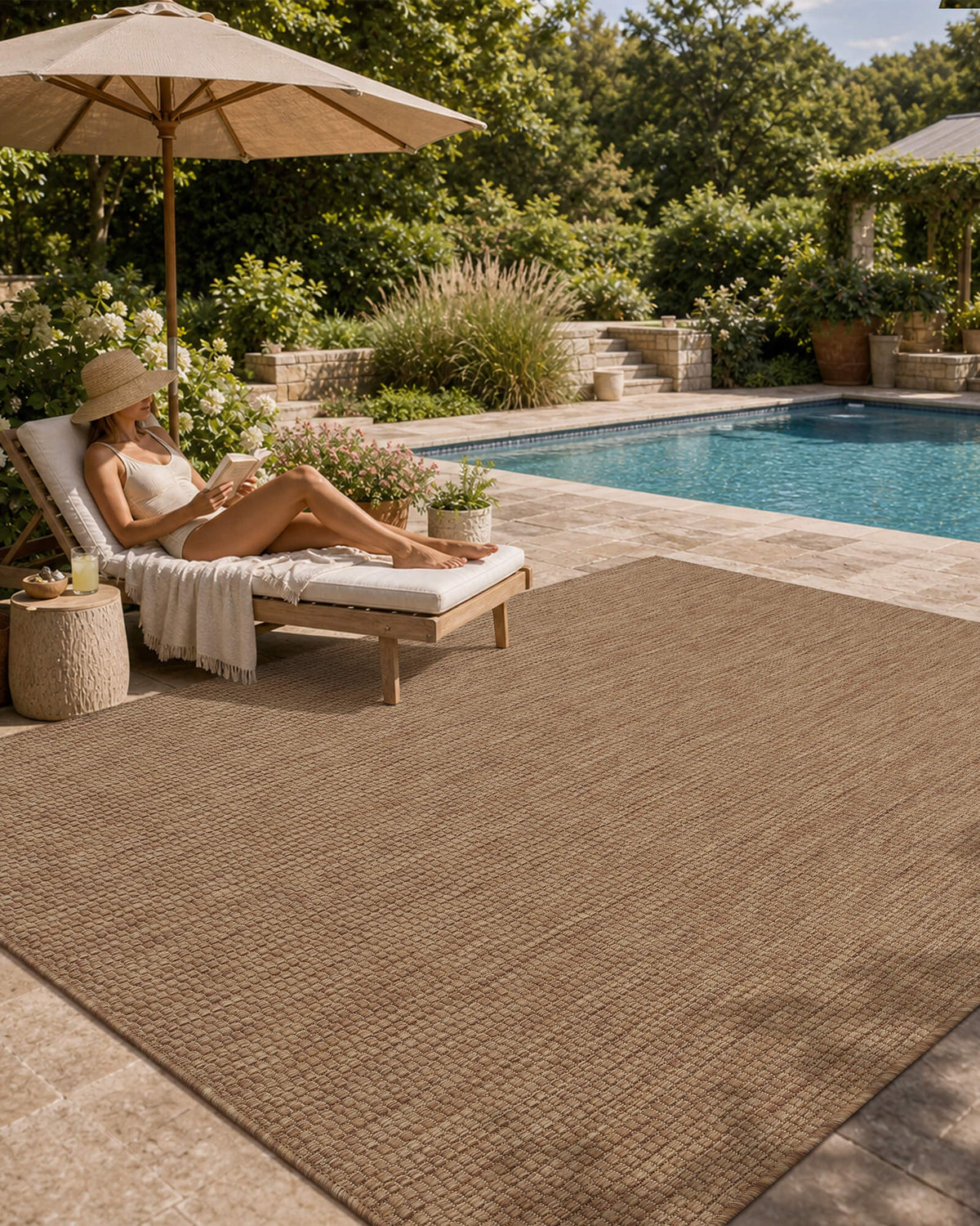 A brown plain weave outdoor area rug creates a relaxed poolside lounge space with a chaise chair, umbrella shade, garden greenery, and weather-resistant patio style for everyday outdoor living.