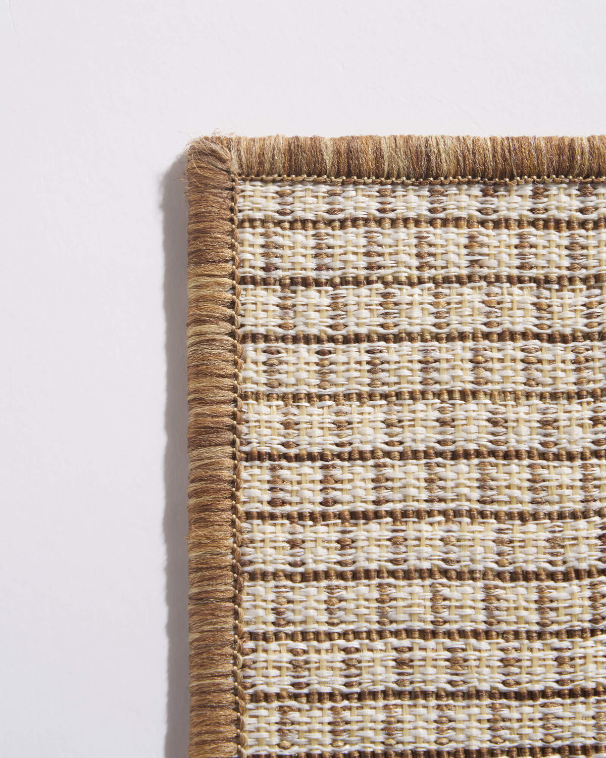 A close-up backside view of a brown plain weave outdoor rug shows its open grid weave, finished border, and durable construction for patios, decks, porches, and outdoor entryways.