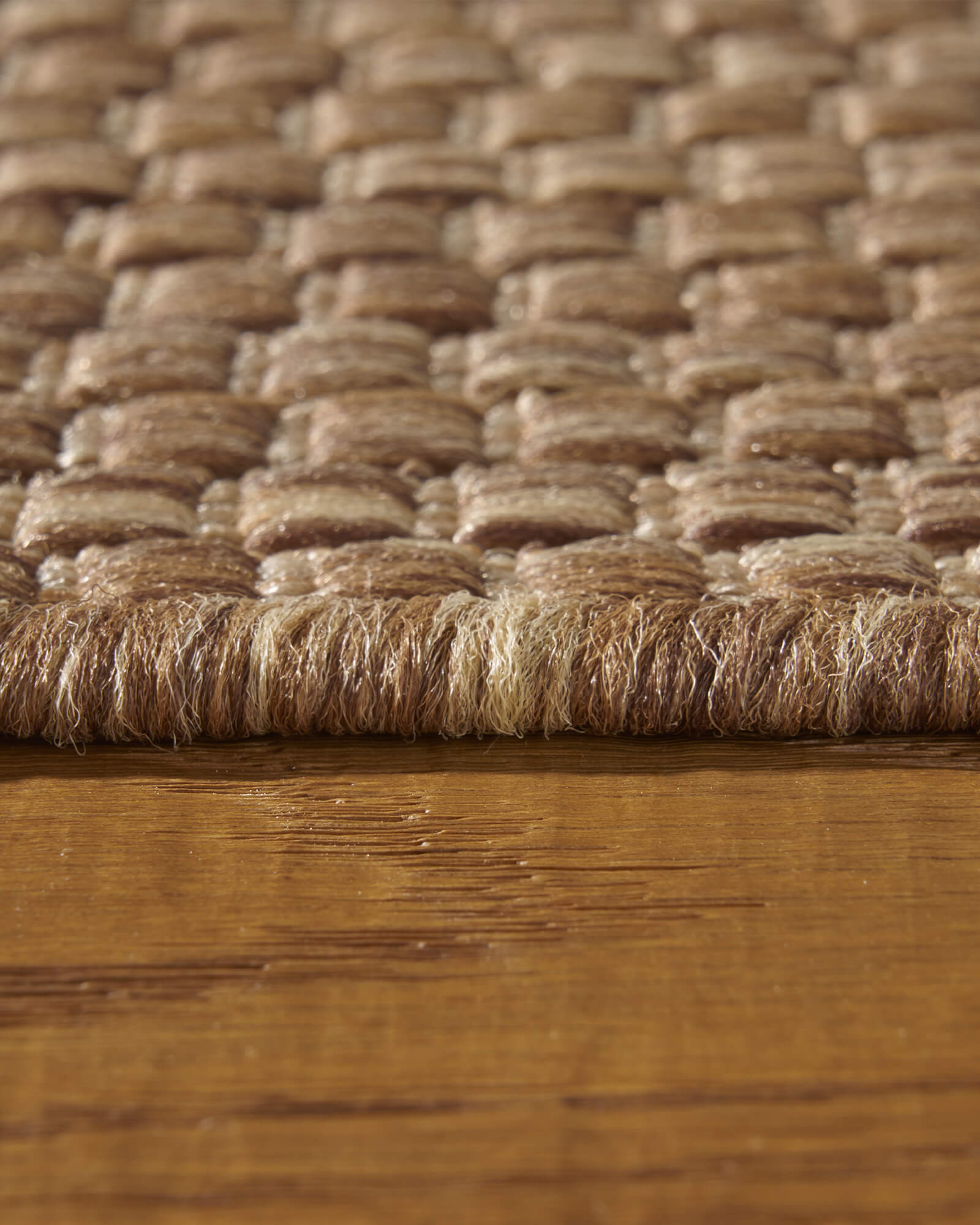 A close-up view of a brown plain weave outdoor rug showing its edge height, chunky basketweave texture, and durable woven surface for patios, decks, porches, and outdoor living spaces.