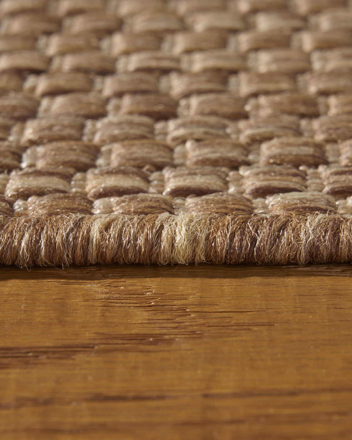 A close-up view of a brown plain weave outdoor rug showing its edge height, chunky basketweave texture, and durable woven surface for patios, decks, porches, and outdoor living spaces.
