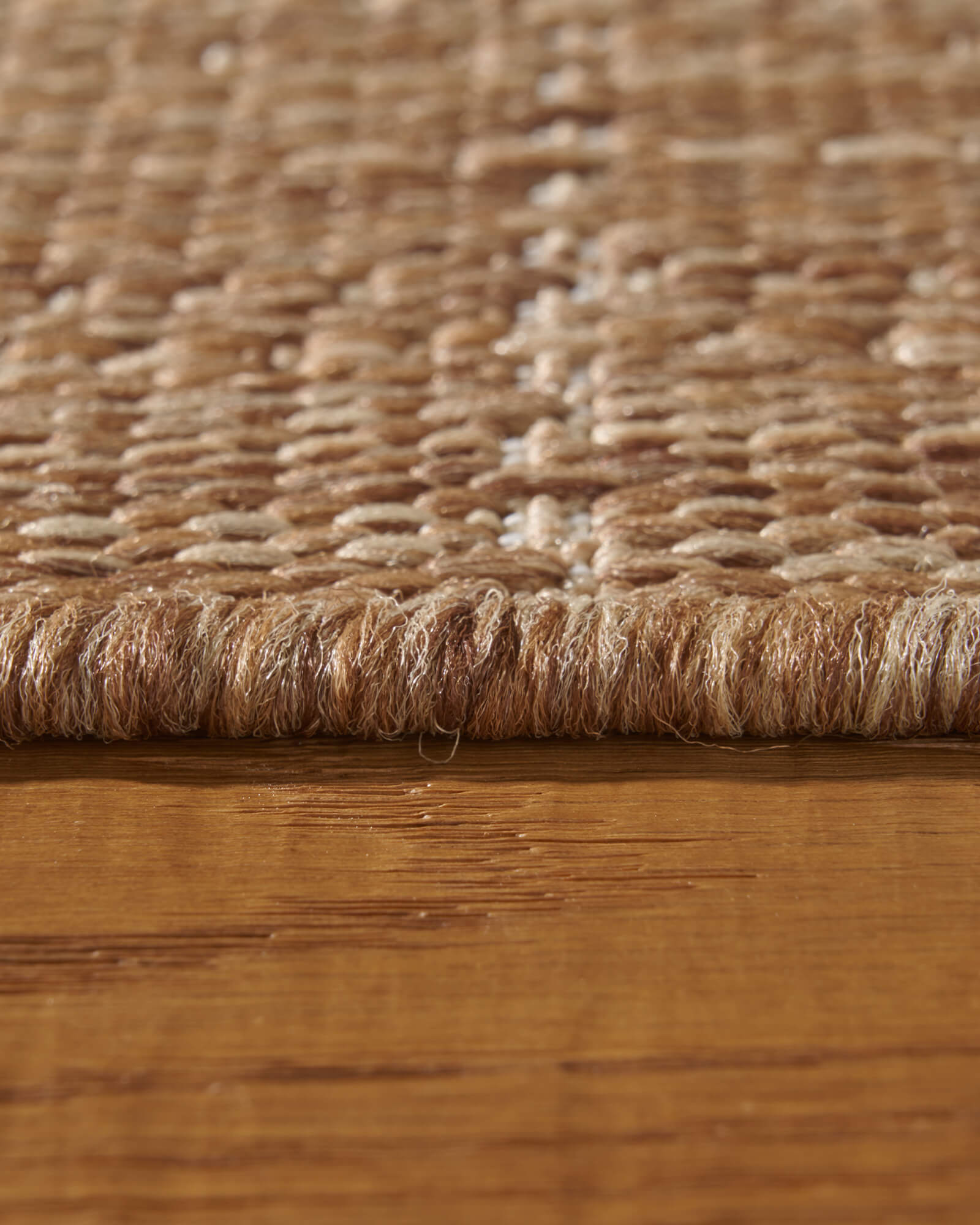 A macro close-up of a brown plain weave outdoor rug shows its thick bound edge, natural woven texture, and durable low-profile surface for patios, decks, porches, and outdoor living spaces.