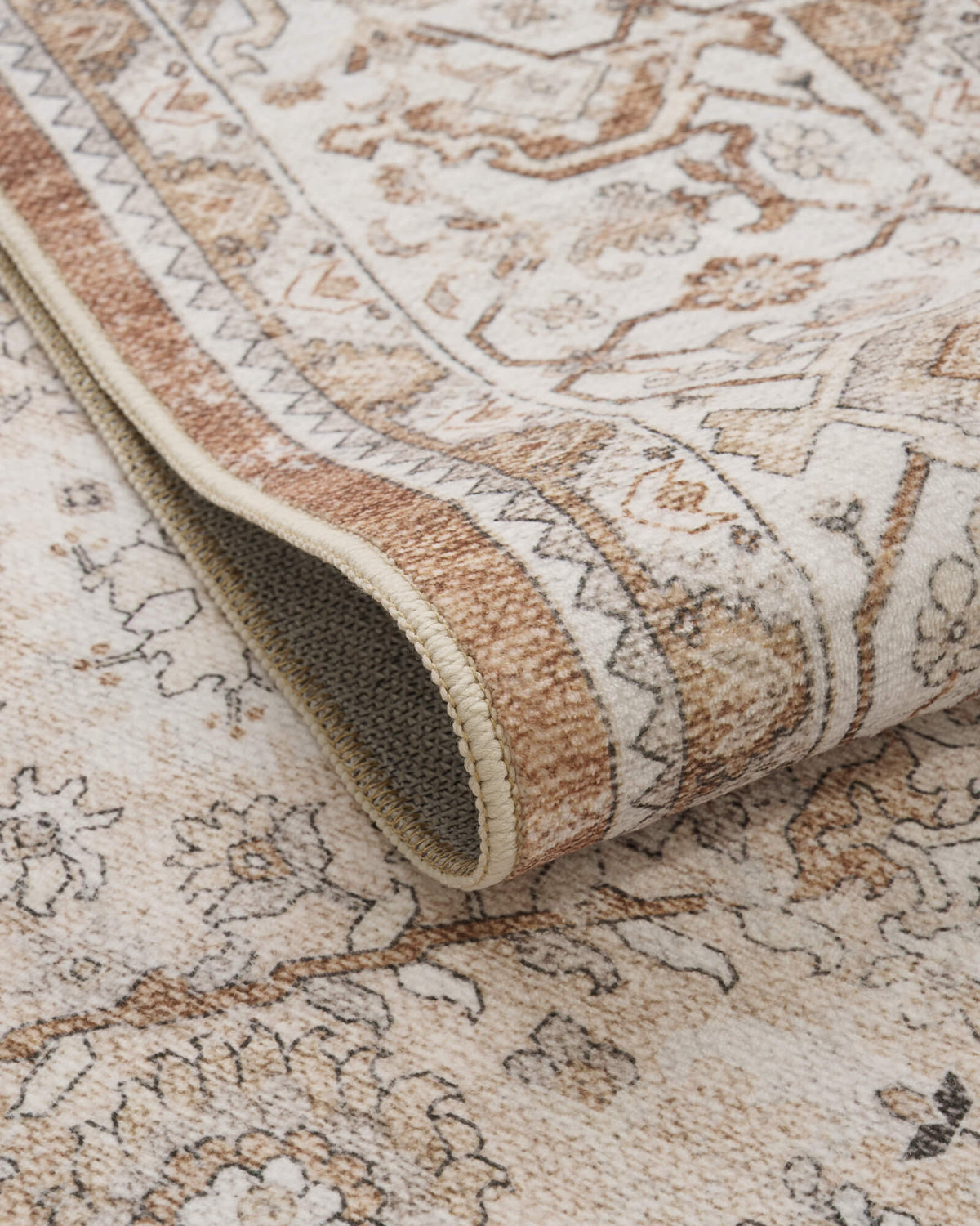 A close-up view of a brown vintage washable area rug showing its curled edge, gray non-slip backing, distressed ornate border, and softly textured surface for cozy living room, bedroom, and dining room decor.