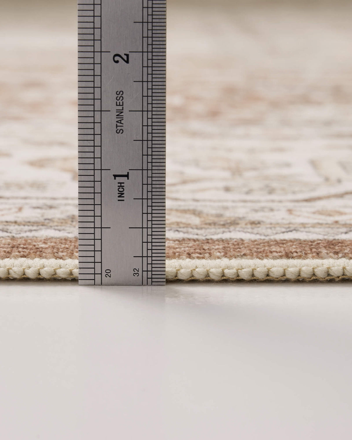 A close-up view of a brown vintage washable area rug showing its ruler-measured pile height, low-profile surface, and neatly bound edge for easy-care living room, bedroom, and family home use.
