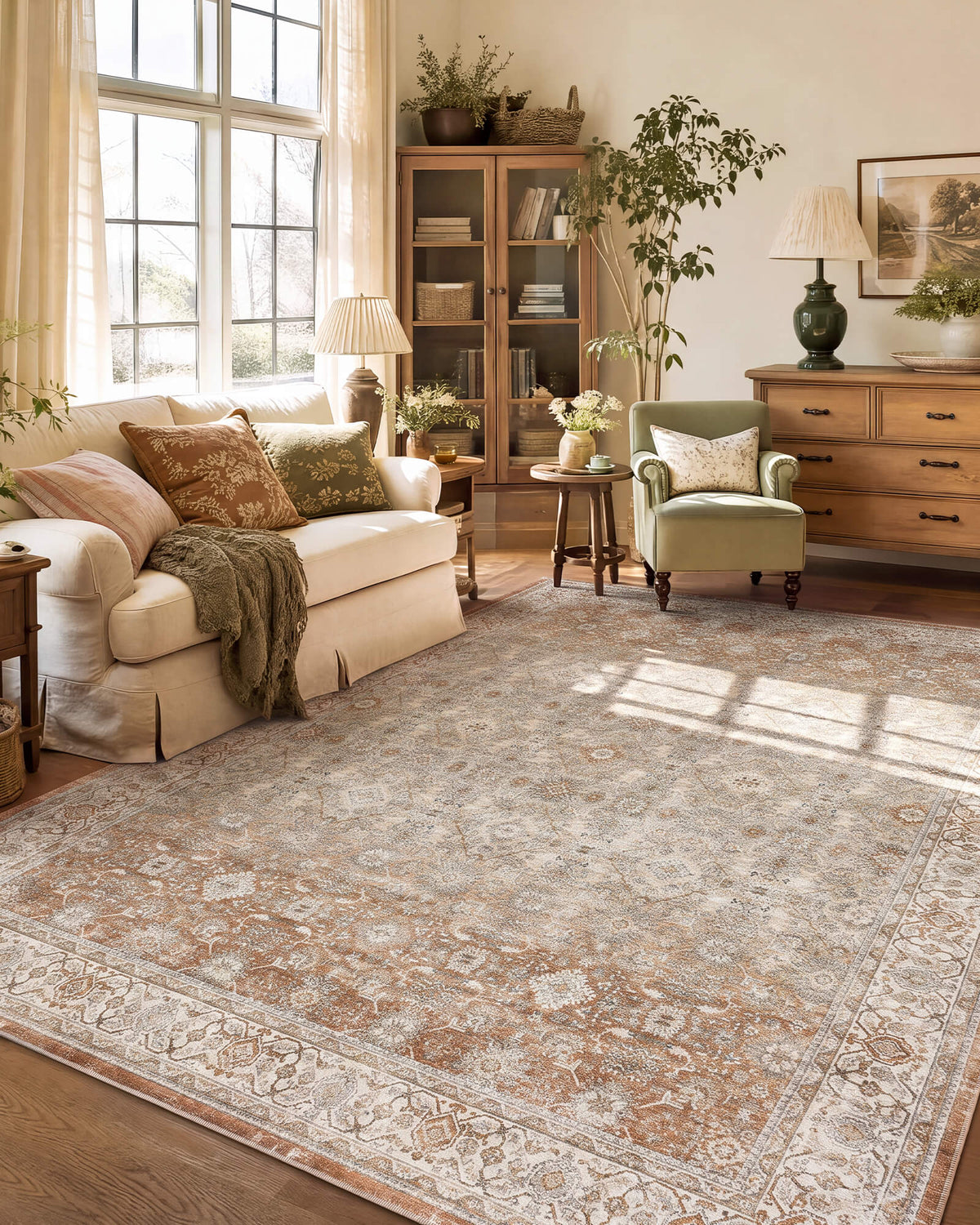 A brown vintage washable area rug with a distressed medallion pattern and ornate border adds warm traditional charm to a sunlit living room with a cream sofa, wood furniture, greenery, and cozy layered decor.