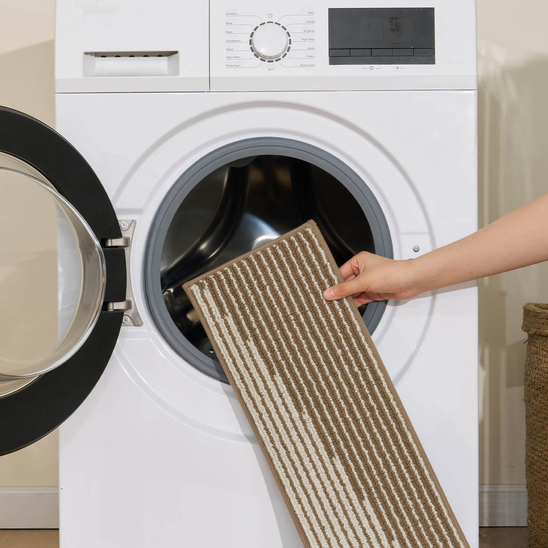 A brown and white striped woven stair tread mat is shown being placed into a front-loading washing machine, highlighting its machine-washable design, soft ribbed texture, and easy-care convenience for keeping indoor wooden stairs clean, comfortable, and stylish.