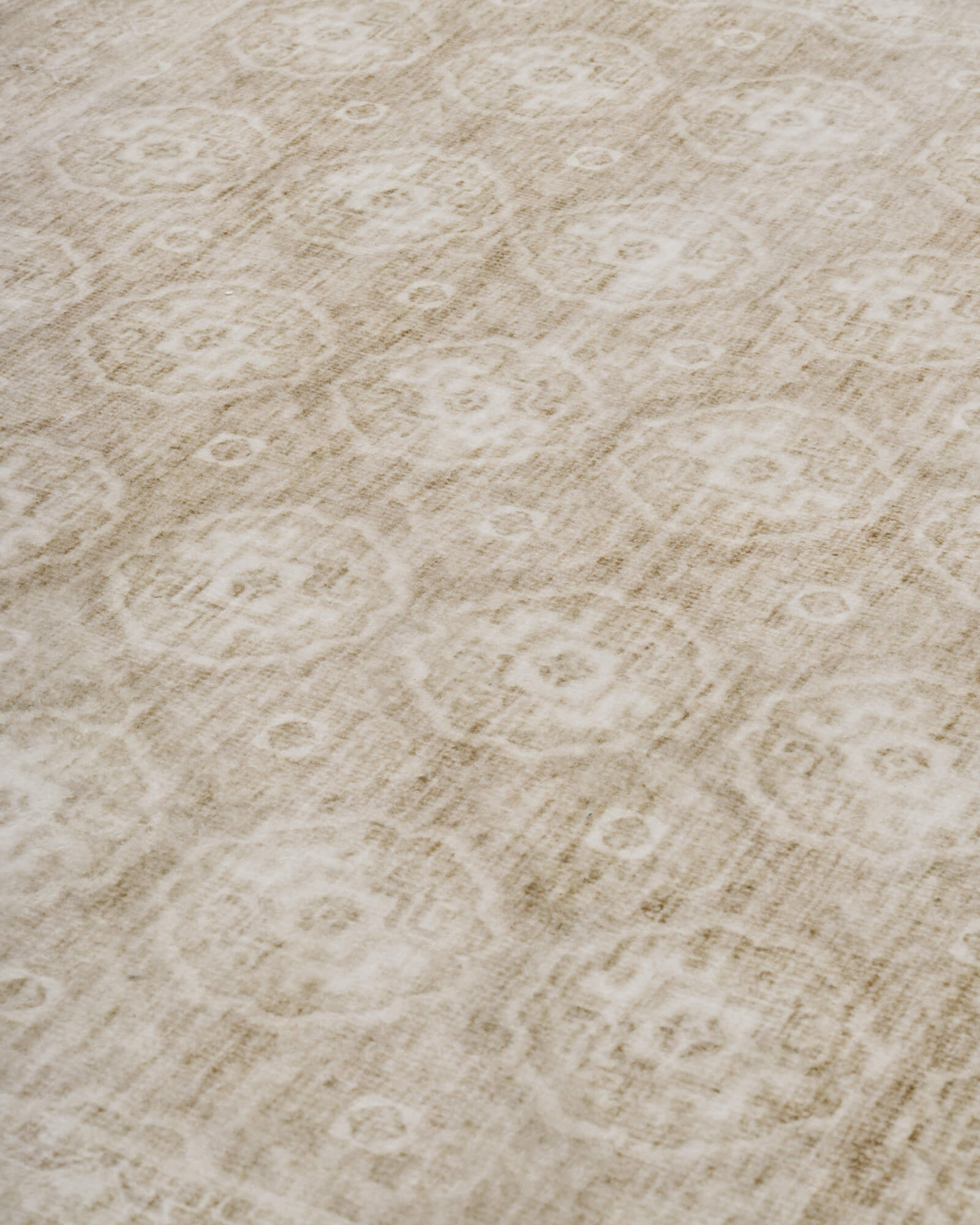 A close-up view of a beige vintage washable area rug highlights its distressed medallion-inspired pattern, soft low-pile surface, and timeless neutral style for living rooms, bedrooms, and dining spaces.