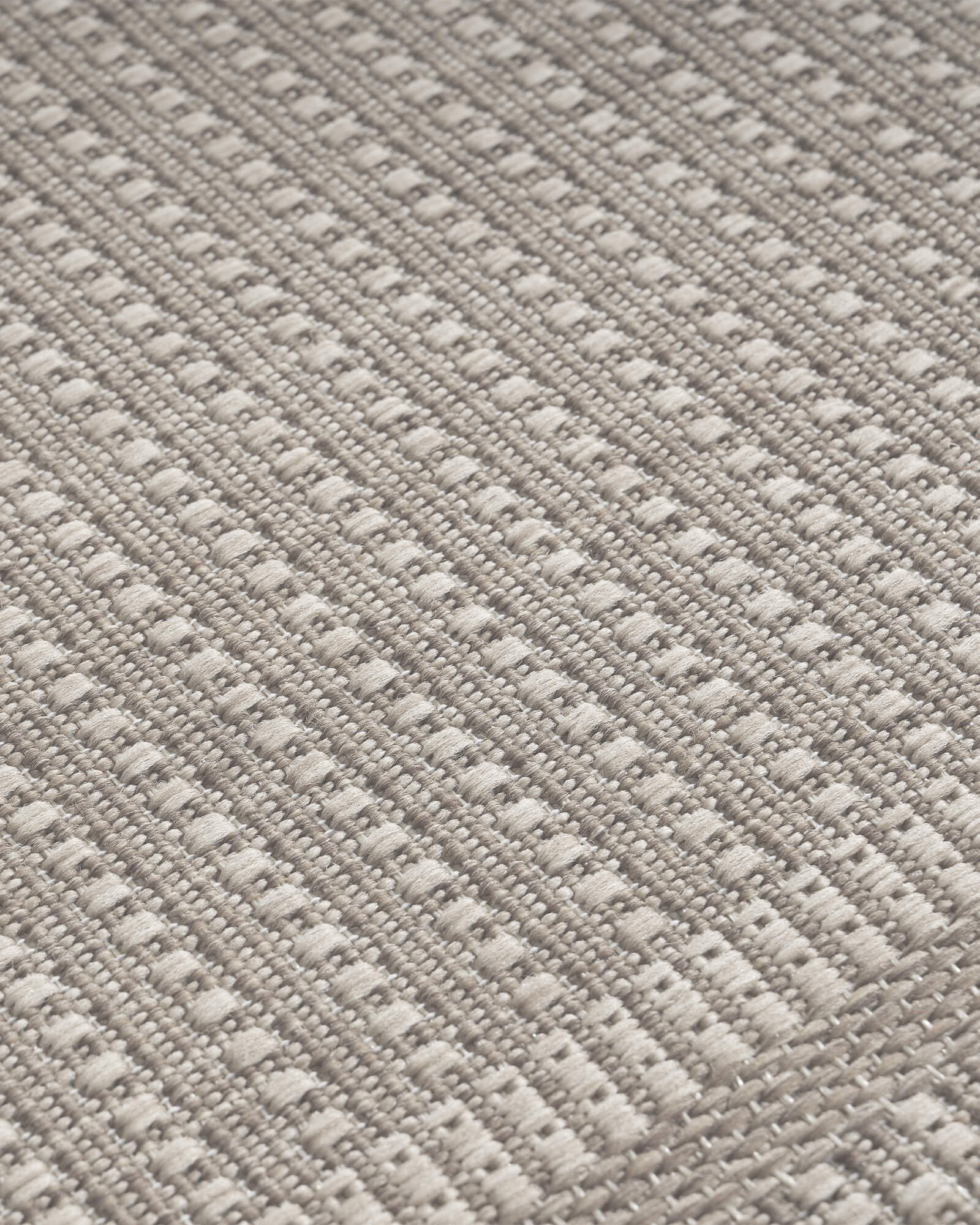 A close-up view of a gray woven indoor outdoor rug shows its durable jute-look texture, low-maintenance surface, and versatile style for patios, porches, kitchens, and indoor living spaces.
