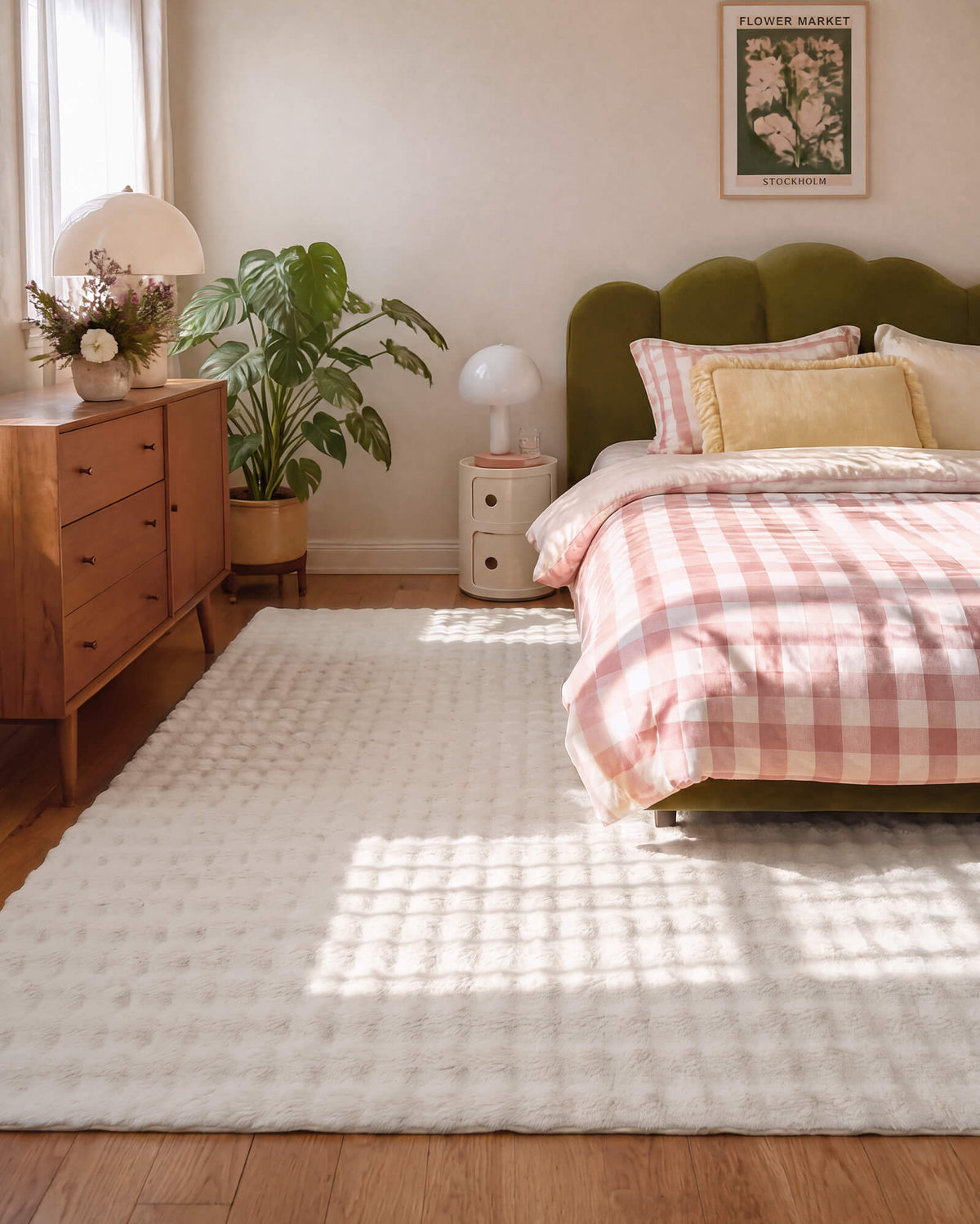 A cream Cloud Soft shag area rug with ultra-fluffy long-pile fibers and a plush checkered texture brings cloud-like softness and luxurious barefoot comfort to a cozy bedroom with an olive green upholstered bed, pink gingham bedding, warm wood furniture, and gentle natural sunlight.