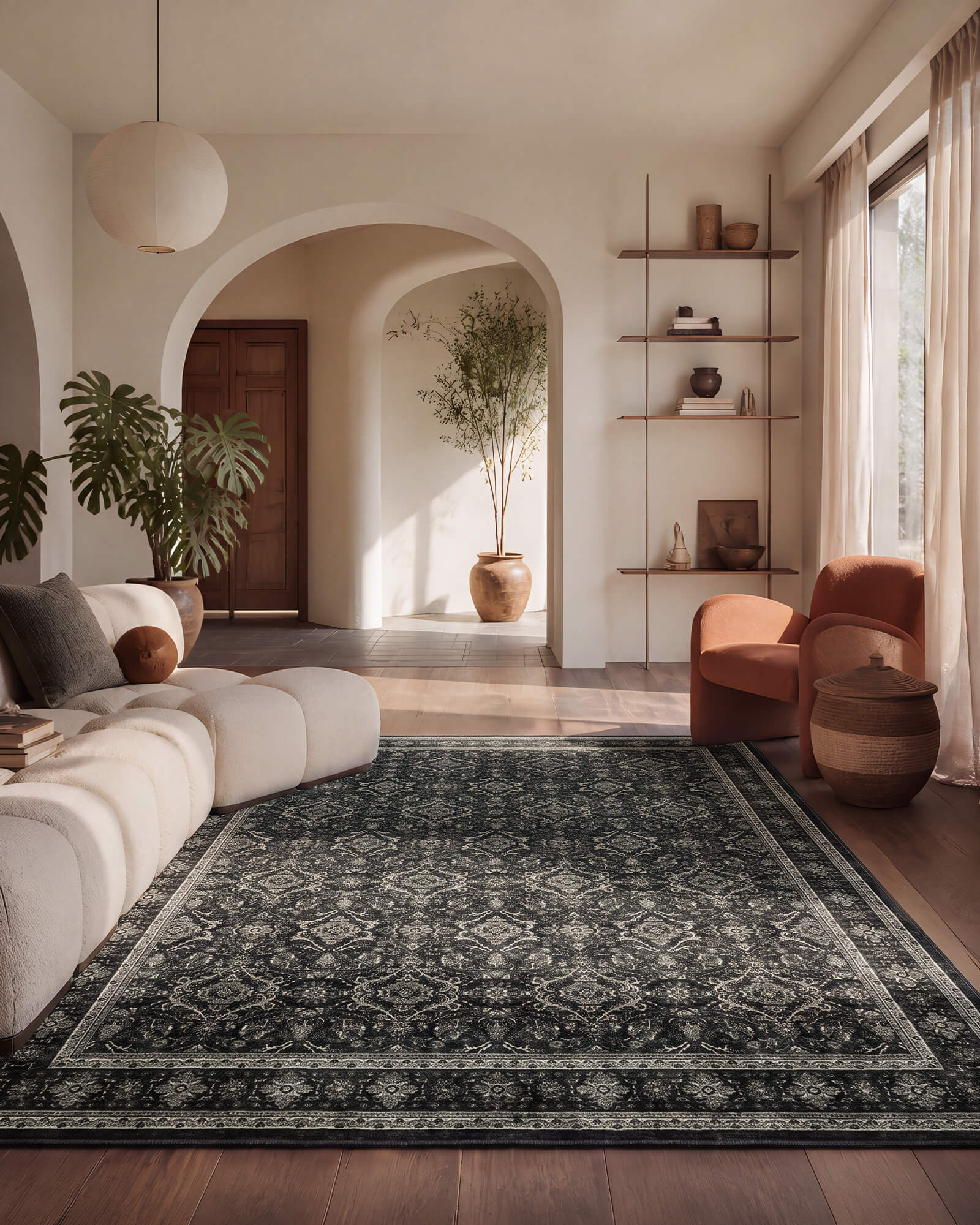 A dark charcoal vintage washable area rug with a faded ornamental border adds rich contrast to an arched living room with a modular sofa, rust accent chair, warm wood floors, and modern boho decor.