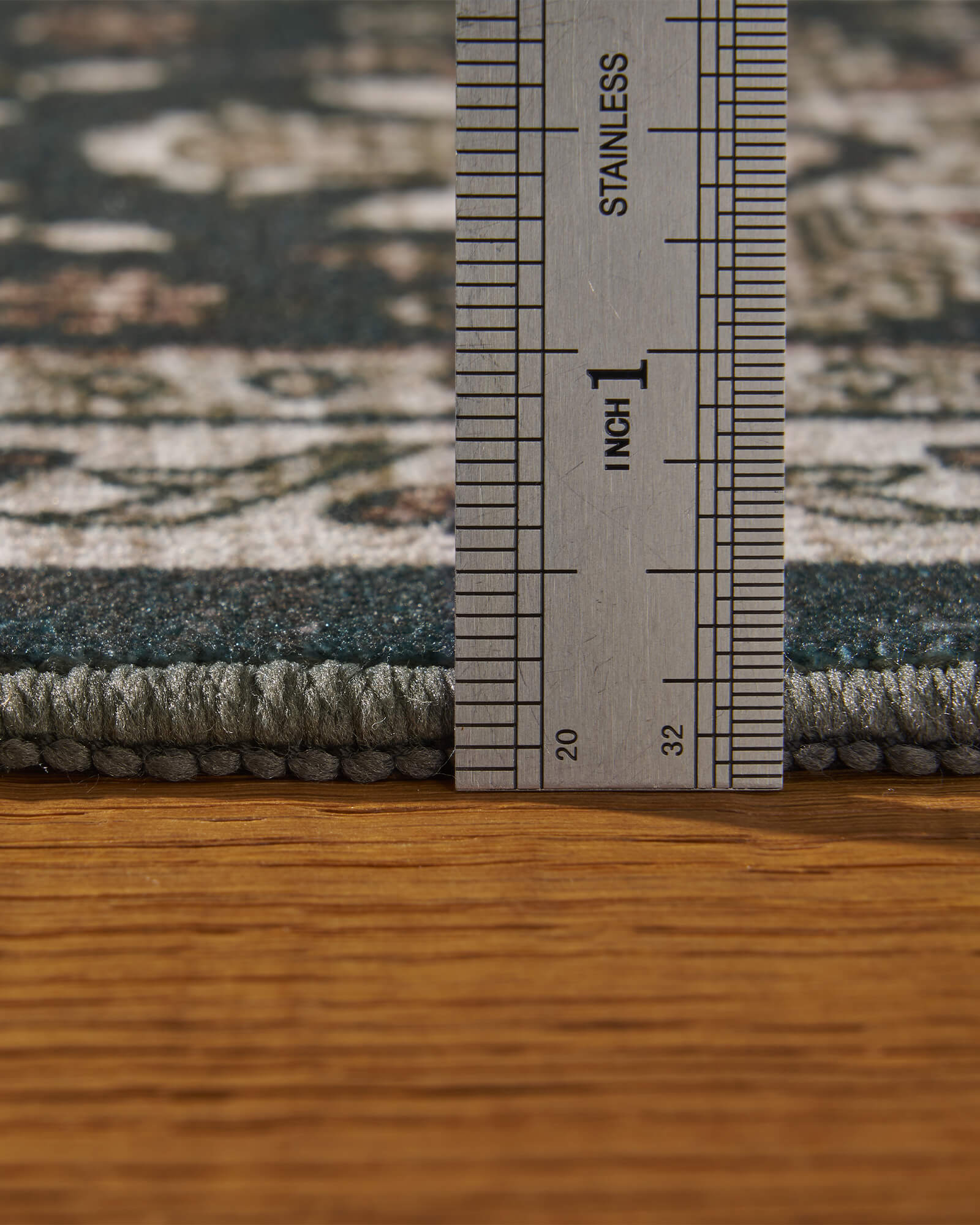 A close-up view of a dark charcoal vintage washable rug showing its ruler-measured thickness, soft low-profile pile, and bound edge for easy placement in living rooms, bedrooms, and high-traffic family spaces