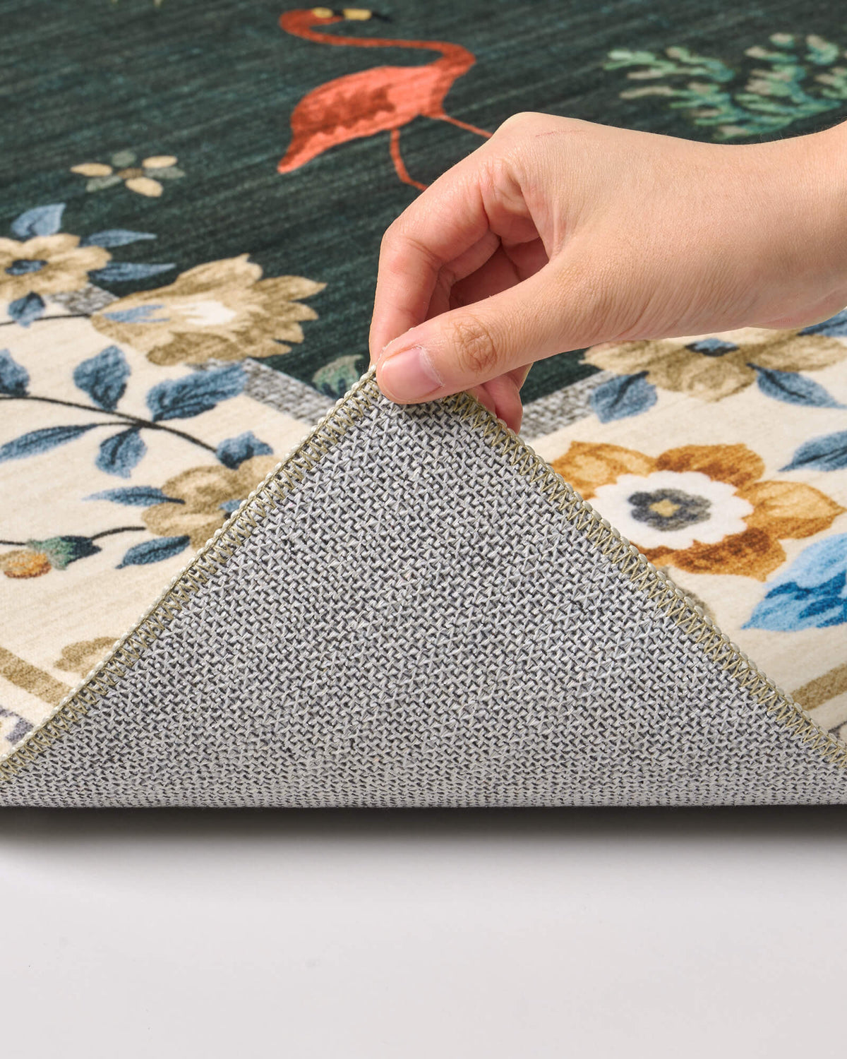 A close-up view of a dark green soft kids rug showing its folded corner, gray non-slip backing, flamingo and floral border pattern, and neatly finished edge for safe, cozy nursery, playroom, and children’s bedroom use.