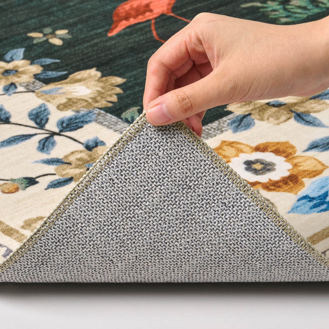 A close-up view of a dark green soft kids rug showing its folded corner, gray non-slip backing, flamingo and floral border pattern, and neatly finished edge for safe, cozy nursery, playroom, and children’s bedroom use.