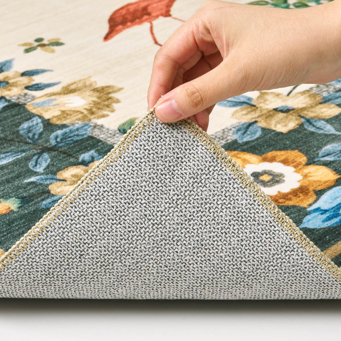 A close-up view of a dark green soft kids rug showing its folded corner, gray non-slip backing, floral border pattern, and neatly finished edge for safe, cozy nursery, playroom, and children’s bedroom use.