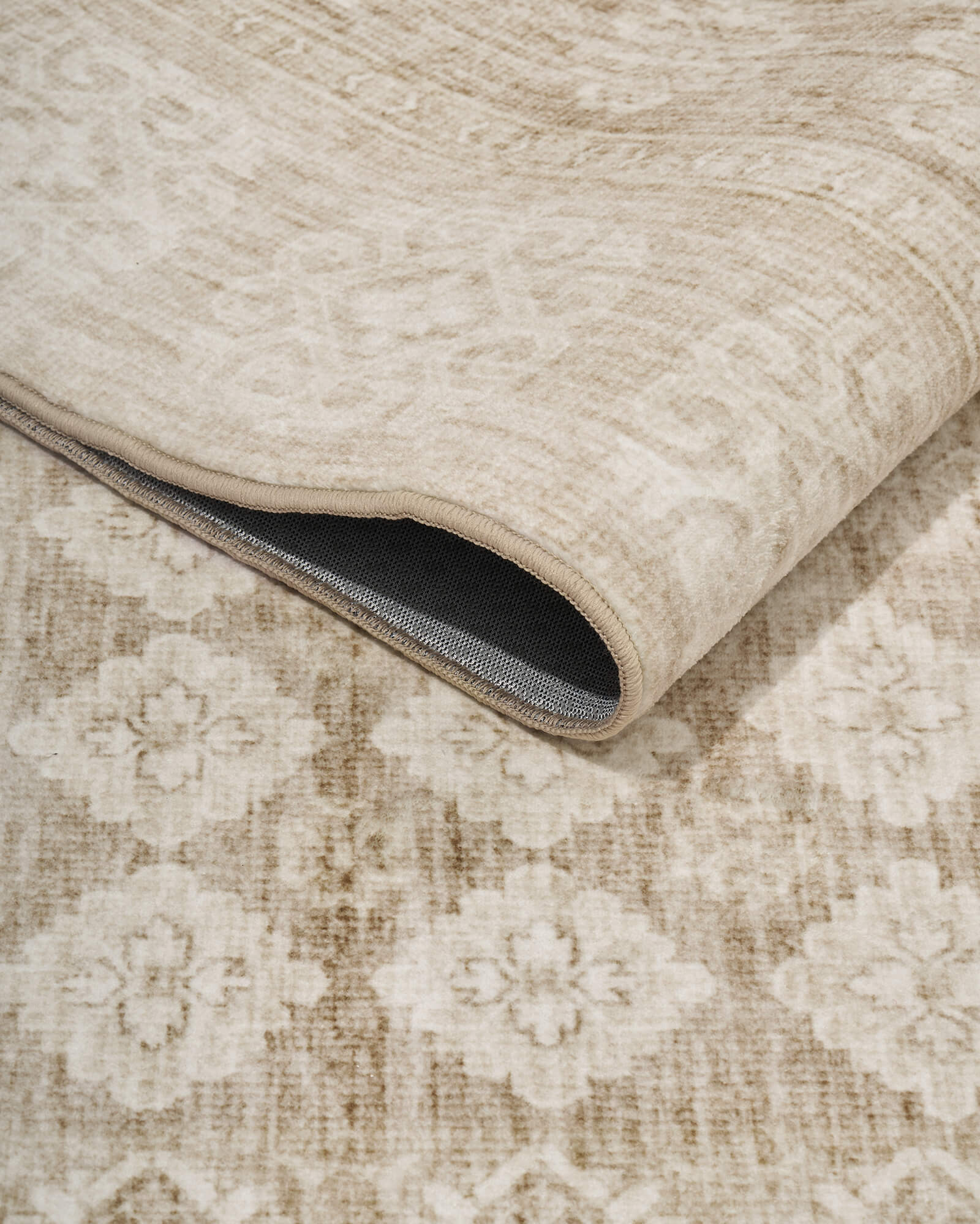 A foldable beige vintage washable area rug features a soft distressed floral surface and non-slip backing, making it easy to clean, move, and style in cozy living rooms, bedrooms, and dining spaces.