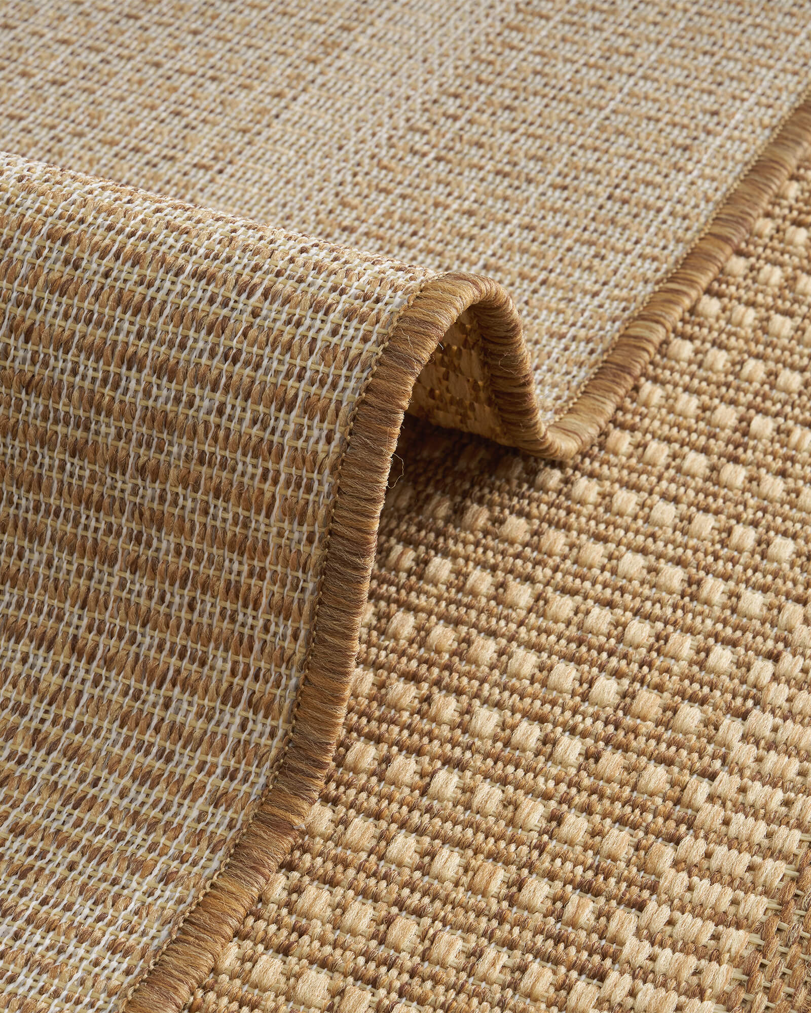 A foldable natural woven indoor outdoor rug features a textured jute-look surface and reinforced edge for durable, easy-care use on patios, porches, and indoor living spaces.