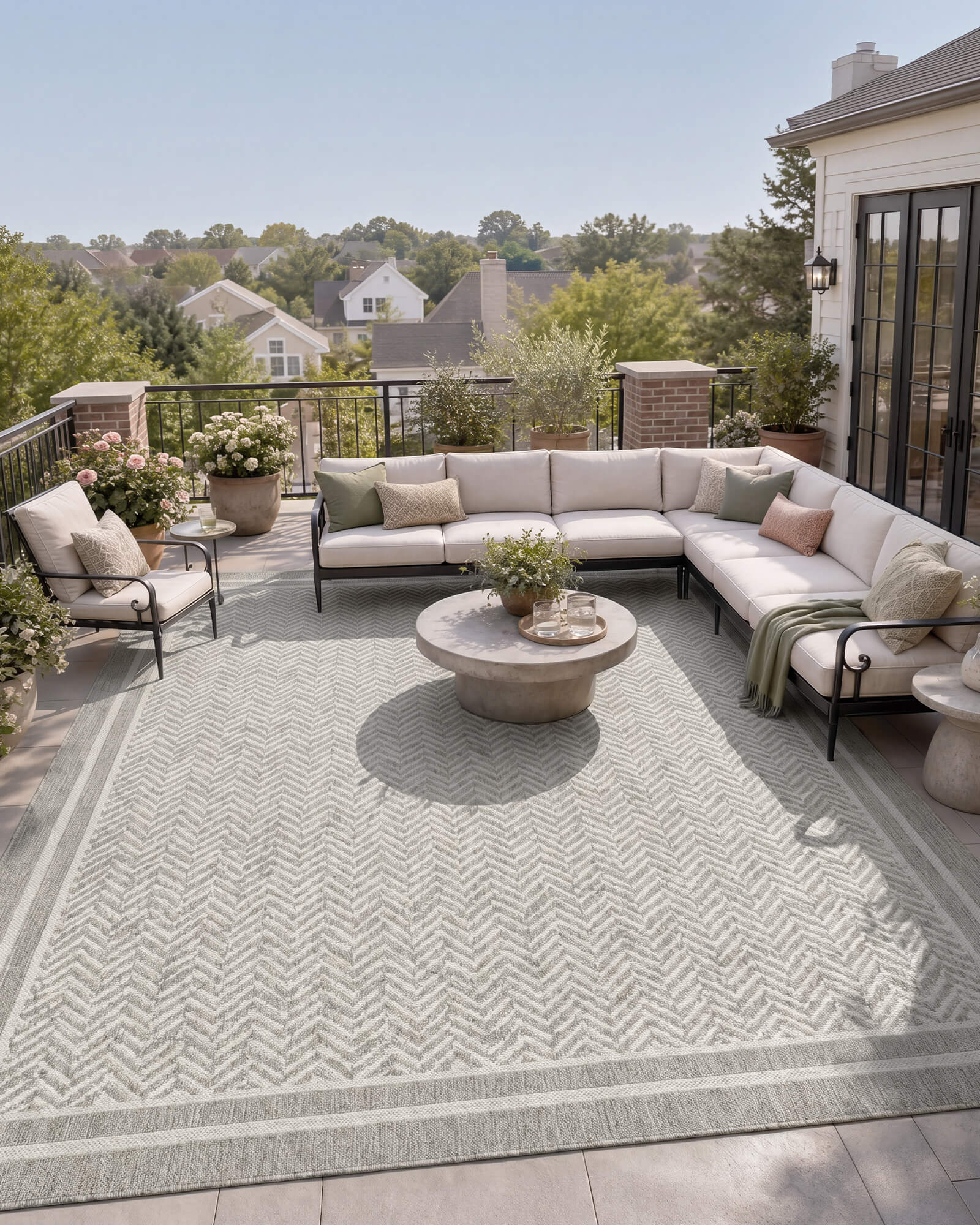 A gray chevron indoor outdoor rug adds durable woven texture and easy-care style to a balcony patio lounge with sectional seating, garden planters, and warm open-air decor.