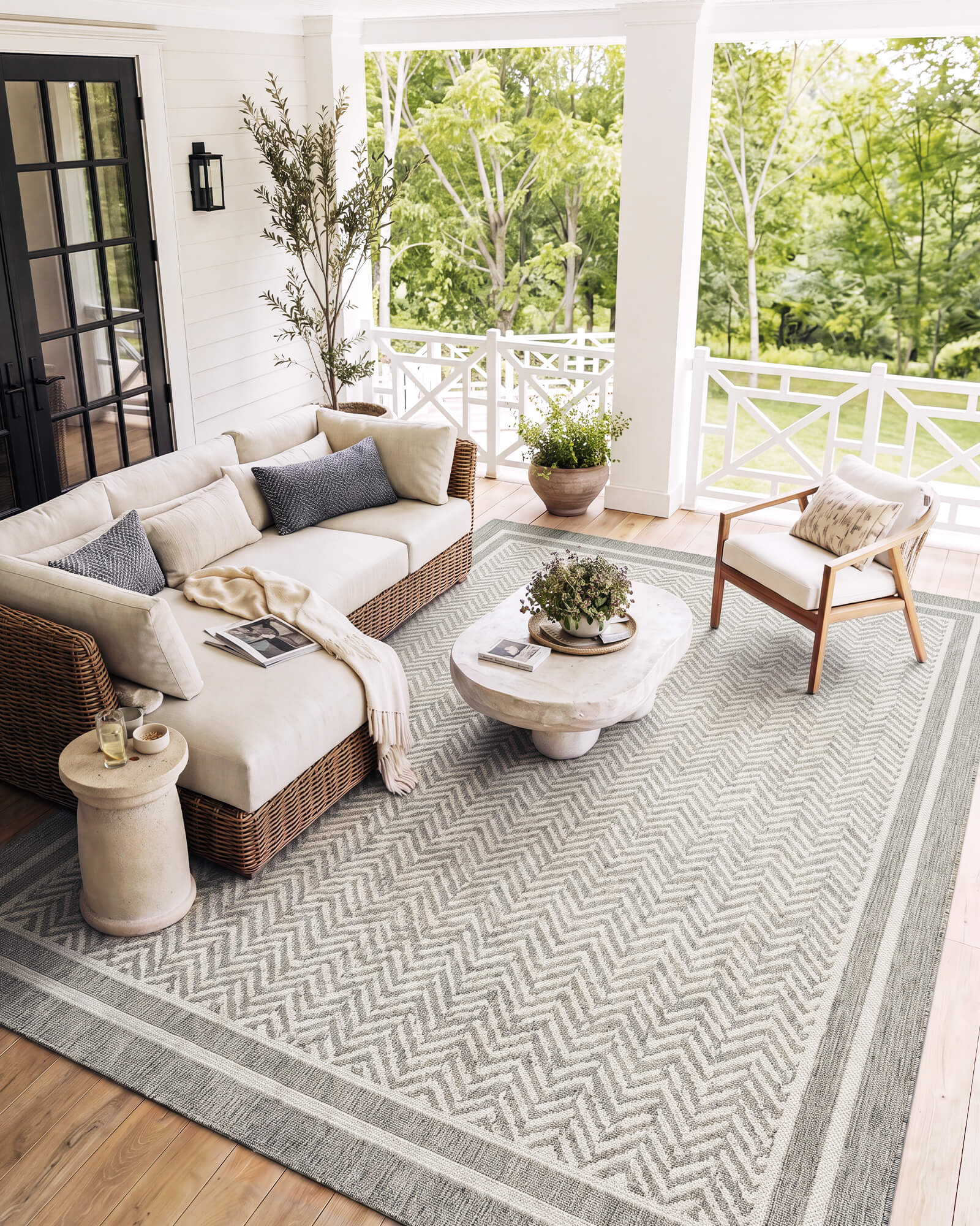 A gray chevron indoor outdoor rug adds durable woven texture and easy-care style to a covered porch lounge with wicker seating, white railings, wood