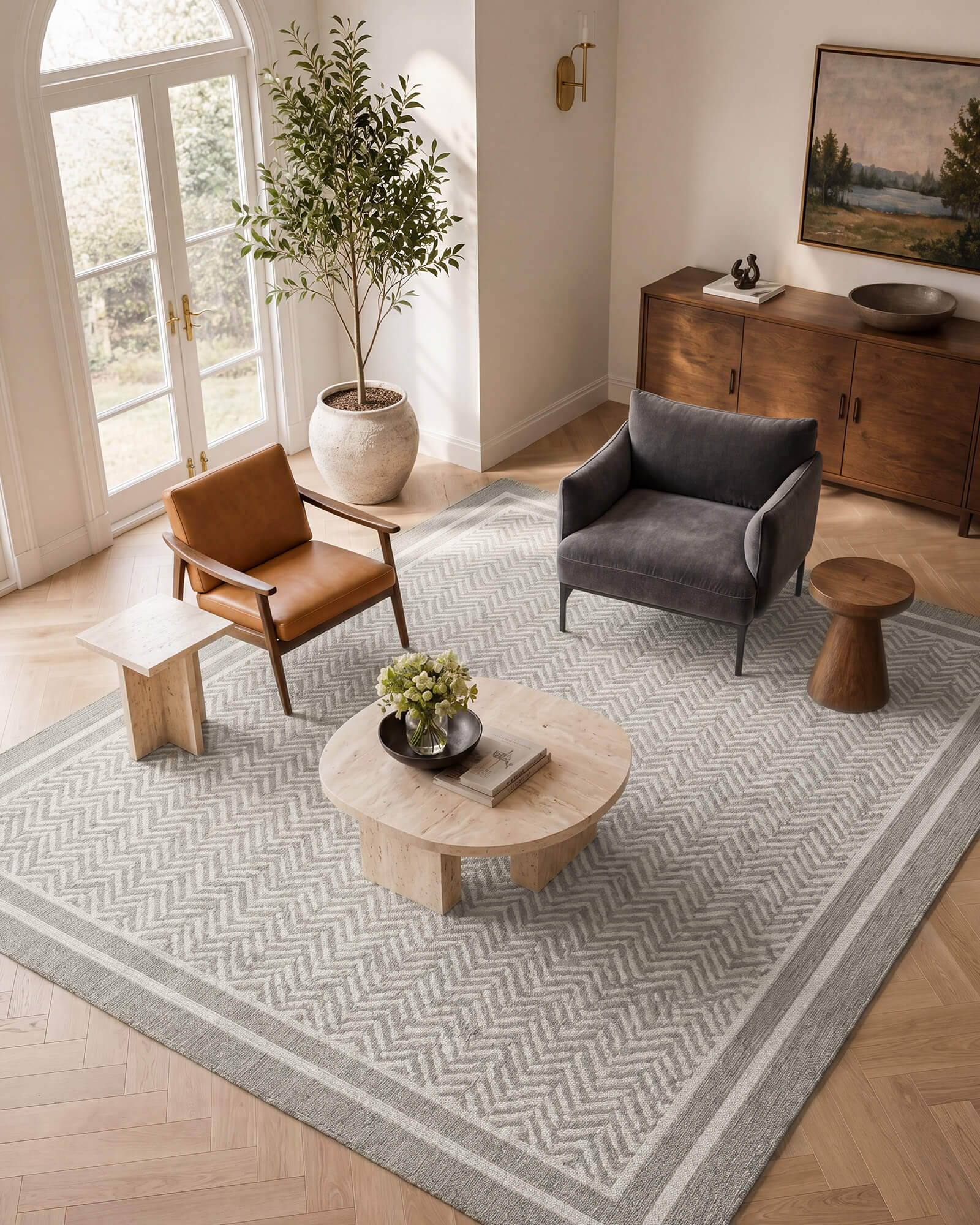 A gray chevron indoor outdoor rug adds durable woven texture and easy-care style to a modern living room with accent chairs, wood furniture, soft natural light, and warm neutral decor.