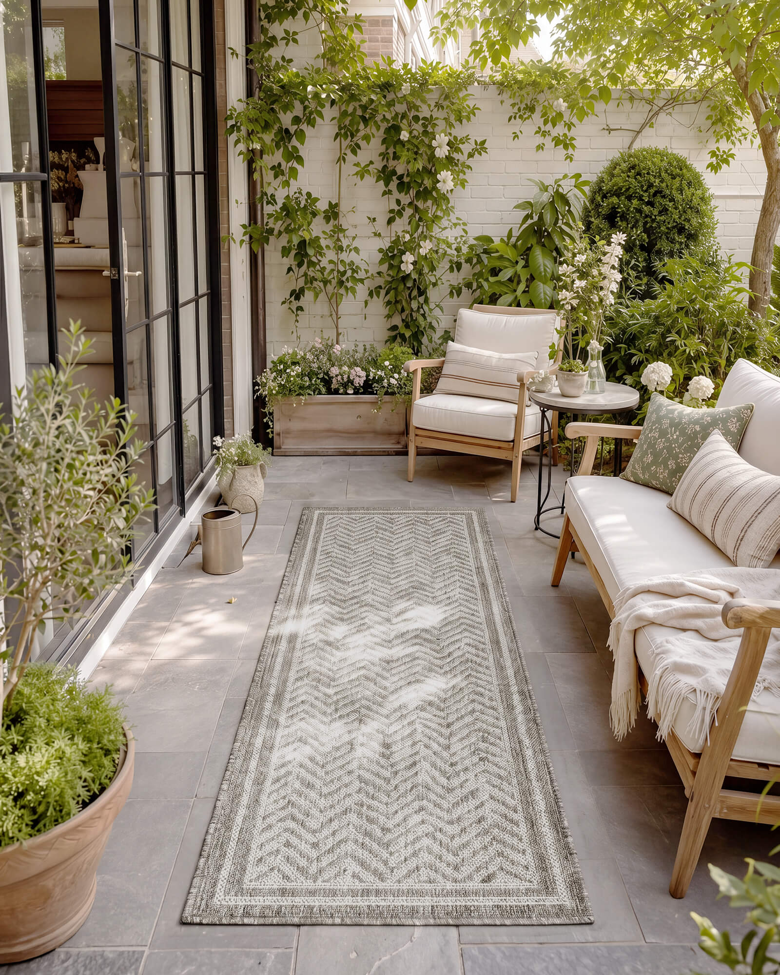 A gray chevron indoor outdoor runner rug adds durable woven texture and easy-care style to a patio walkway with outdoor seating, garden greenery, and soft natural shade.
