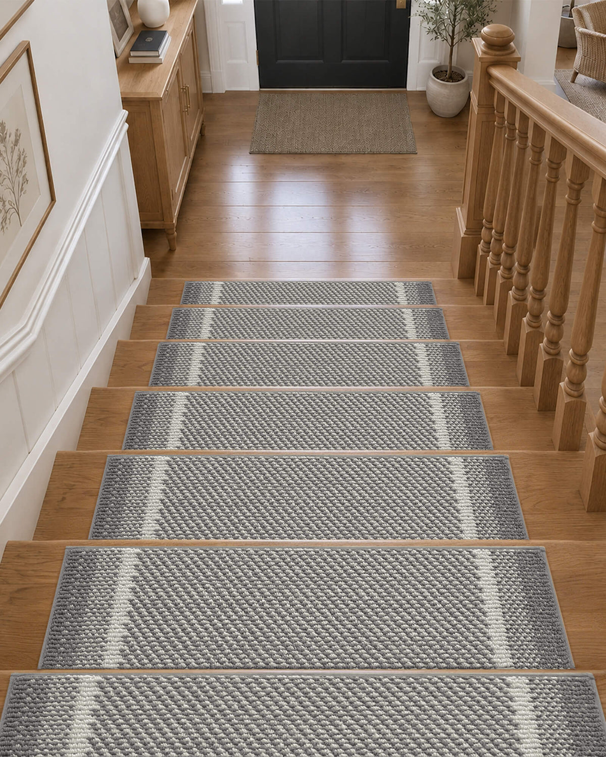 Gray gradient striped non-slip stair treads neatly line a wooden staircase leading to a welcoming entryway, featuring a soft raised woven texture, subtle white accent stripes, and neatly bound edges that provide comfortable footing, help protect hardwood steps, and add modern, understated style to everyday home interiors.