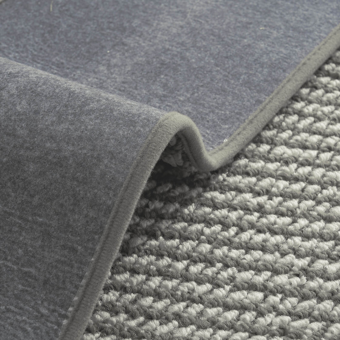 A close-up of gray gradient striped woven stair treads highlights their raised textured surface, soft cushioned loops, flexible gray non-slip backing, and neatly bound edges, offering comfortable footing, reliable grip, and practical protection for indoor wooden staircases.