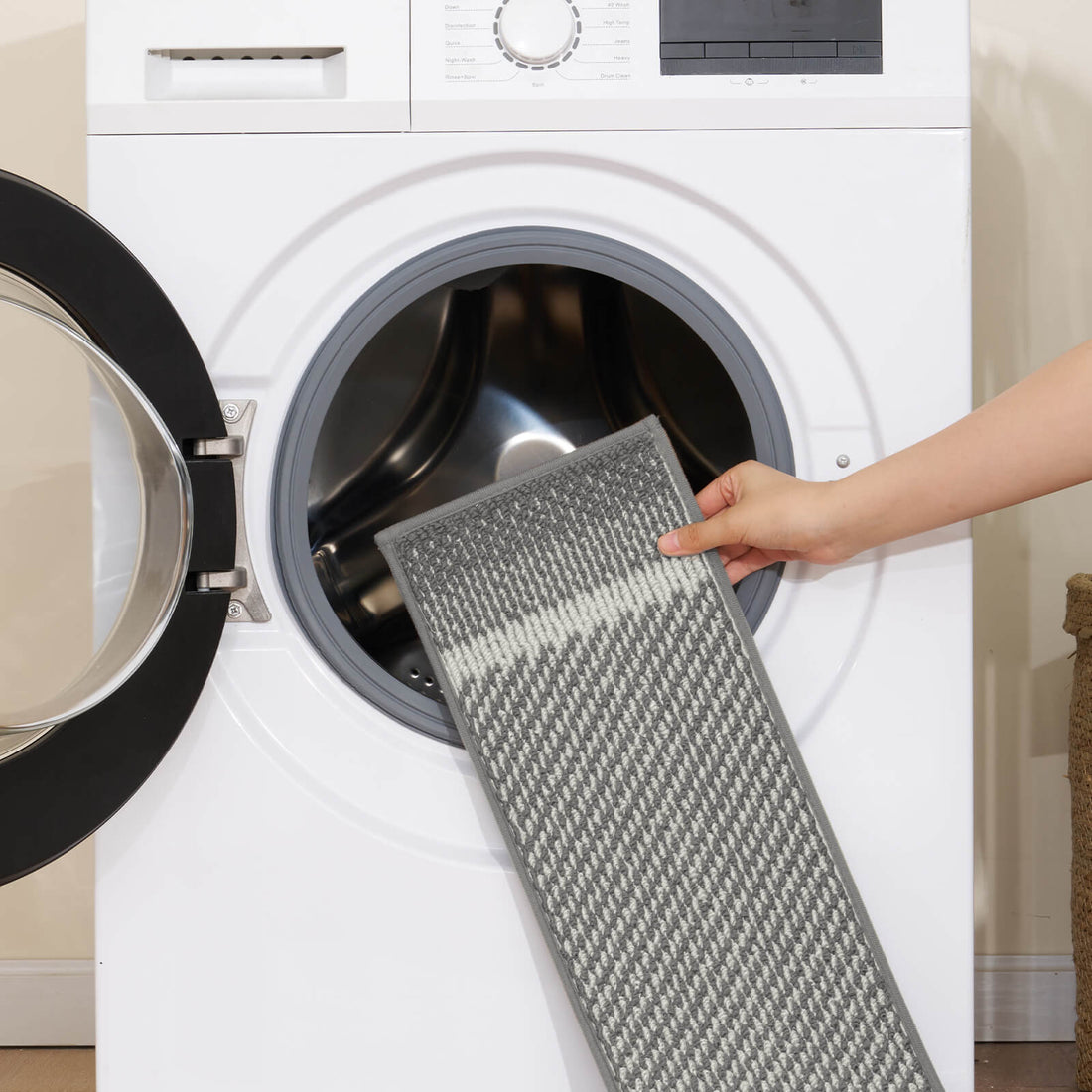 A gray gradient striped woven stair tread mat is shown being placed into a front-loading washing machine, highlighting its machine-washable design, soft textured surface, and modern ombre stripe pattern for easy-care comfort and practical protection on indoor wooden stairs.