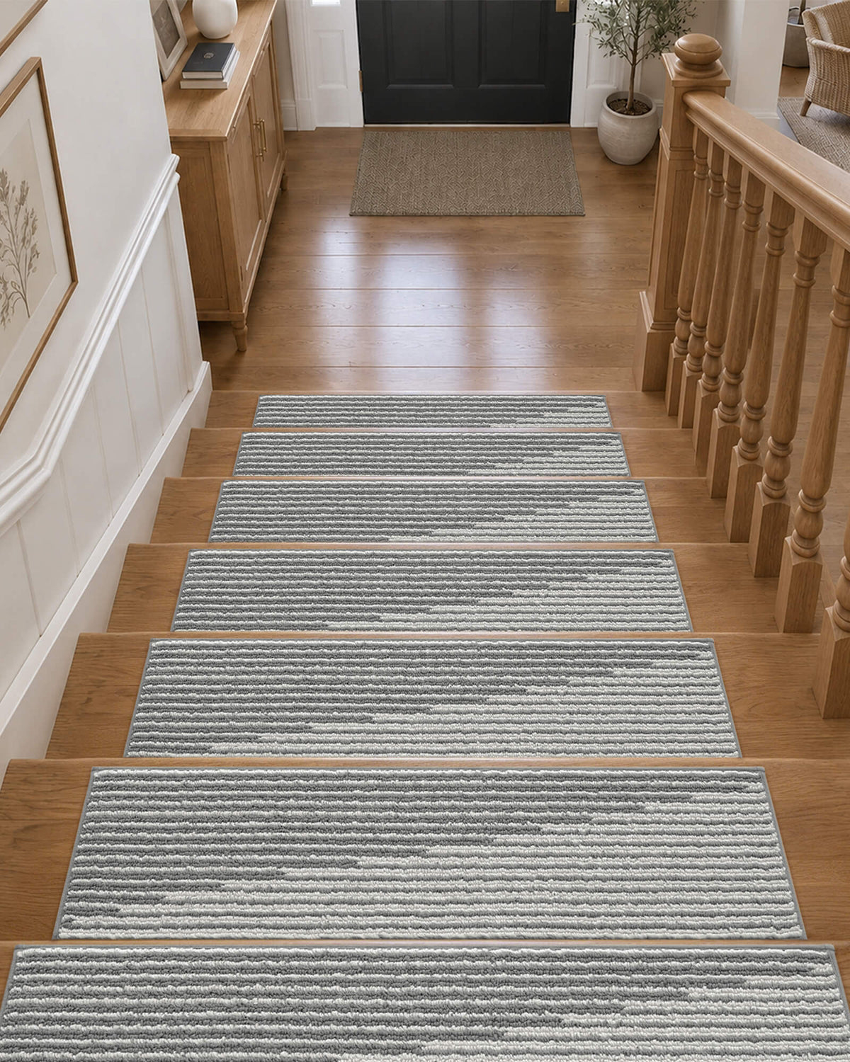Gray and white striped non-slip stair treads neatly line a wooden staircase leading to a welcoming entryway, featuring a soft ribbed woven texture, clean bound edges, and a modern linear pattern that provides comfortable footing, helps protect hardwood steps, and adds understated style to everyday home interiors.