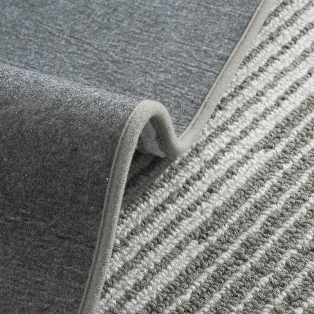 A close-up of gray and white striped woven stair treads highlights their raised ribbed texture, soft cushioned surface, flexible non-slip backing, and neatly bound edges, offering comfortable footing, reliable grip, and practical protection for indoor wooden staircases.