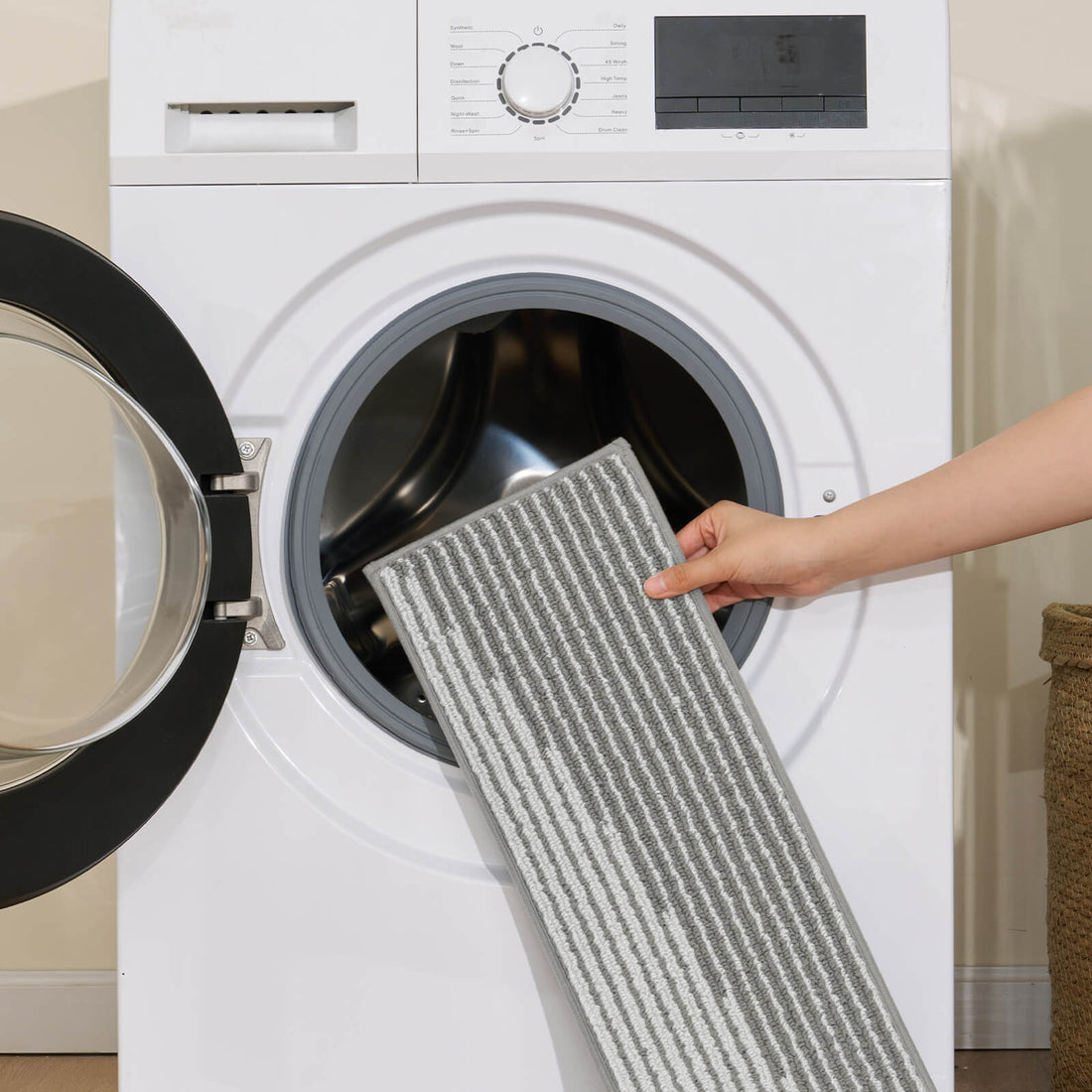 A gray and white striped woven stair tread mat is shown being placed into a front-loading washing machine, highlighting its machine-washable design, soft ribbed texture, and easy-care convenience for keeping indoor wooden stairs clean, comfortable, and stylish.