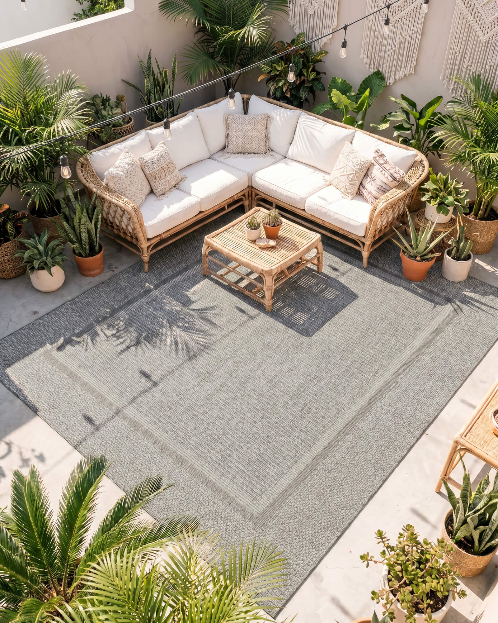 A gray woven indoor outdoor rug adds durable jute-look texture and easy-care style to a patio seating area with rattan furniture, tropical plants, and cozy outdoor decor.