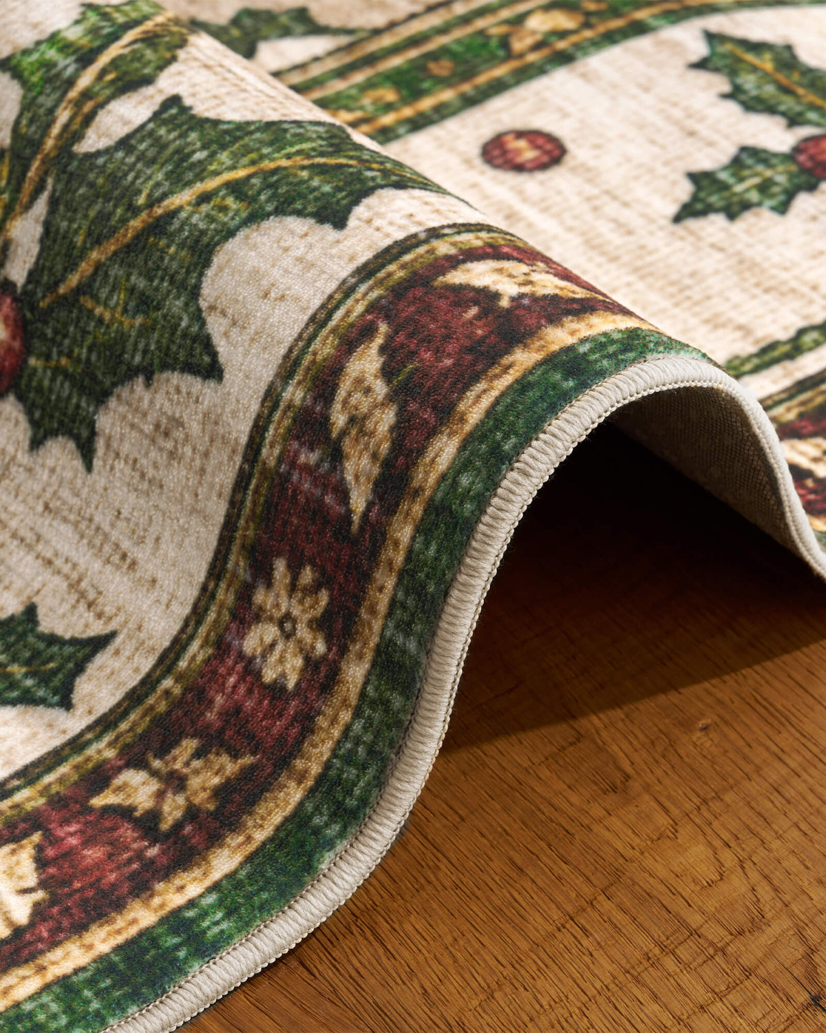A close-up of a green Christmas vintage washable area rug showcases its gently curled edge, soft low-pile surface, neatly bound finish, and festive holly leaf and ornamental border details in rich green, burgundy, and cream tones, highlighting its flexible construction and nostalgic holiday charm for cozy Christmas home decor.
