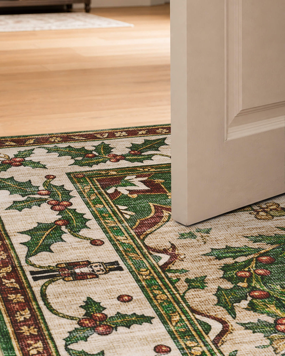 A close-up of a green Christmas vintage washable area rug beneath an interior door highlights its low-profile design, neatly finished edges, and festive holly berry and nutcracker border. Its vintage-inspired pattern brings traditional Christmas charm to doorways, entryways, and cozy holiday living spaces.