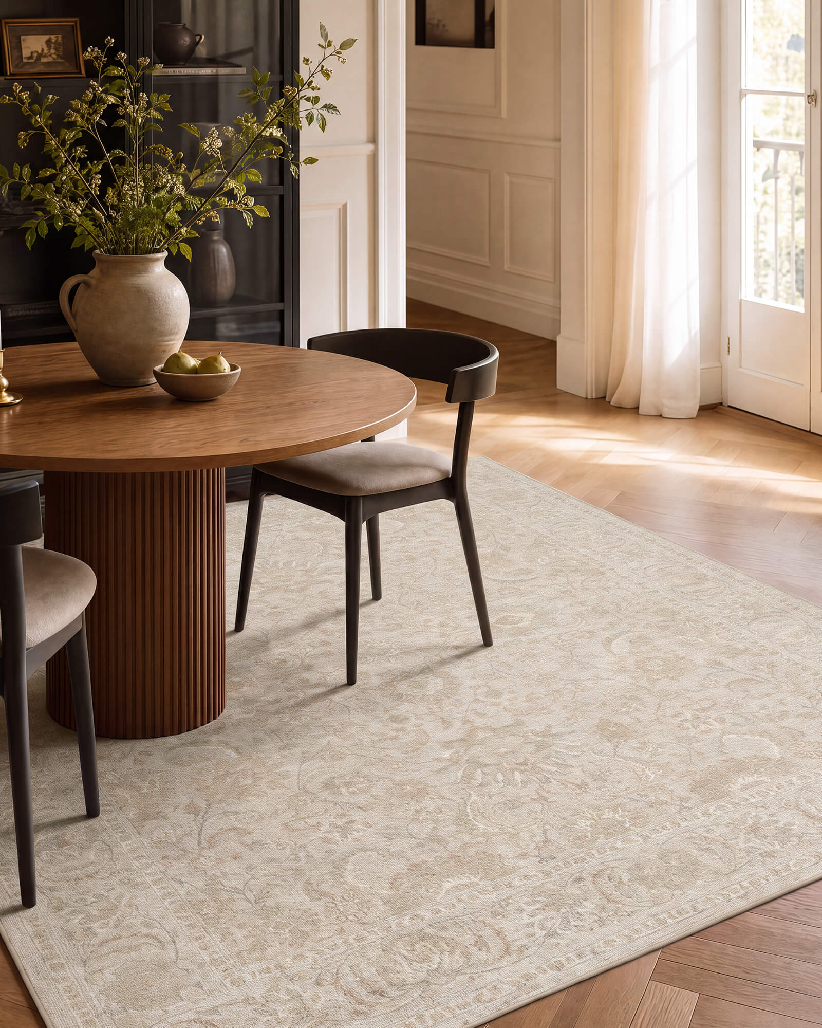 An ivory beige vintage washable rug with a soft distressed ornamental pattern adds elegant texture to a dining room with a round wood table, black chairs, warm sunlight, and refined neutral decor.