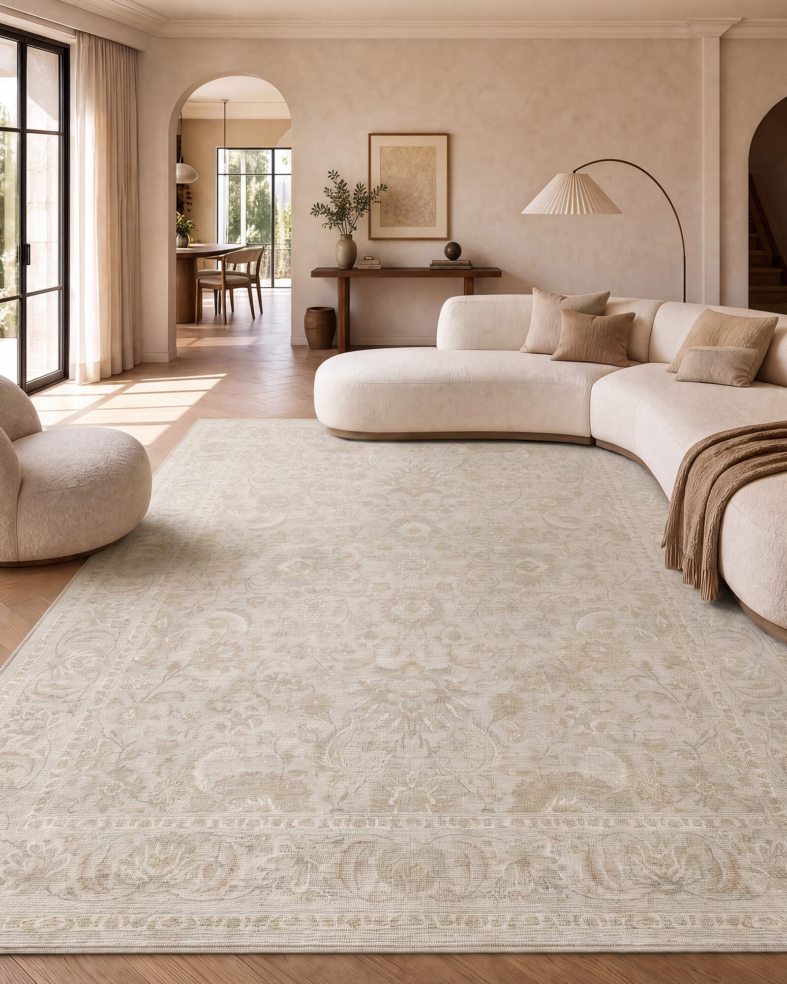 An ivory beige vintage washable rug with a soft ornamental border pattern brings calm, elegant style to a warm living room with a curved sectional sofa, neutral decor, and natural sunlight.