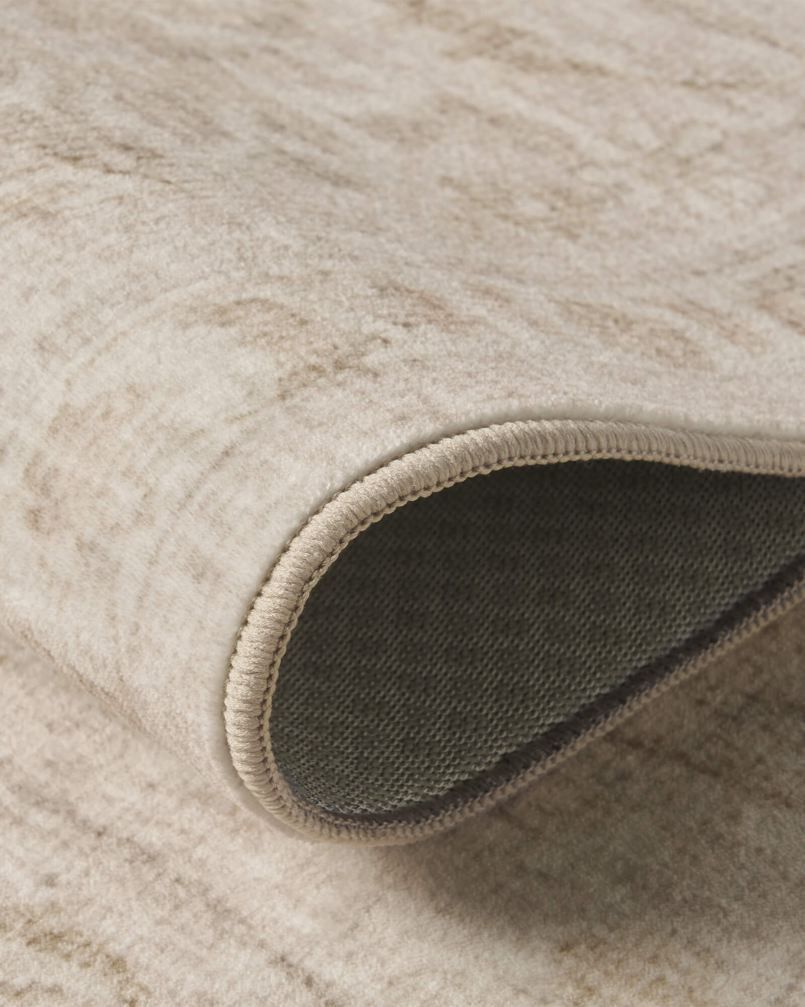 A close-up view of an ivory beige vintage washable rug showing its folded edge, gray backing, soft distressed surface, and flexible low-pile design for cozy everyday home use.
